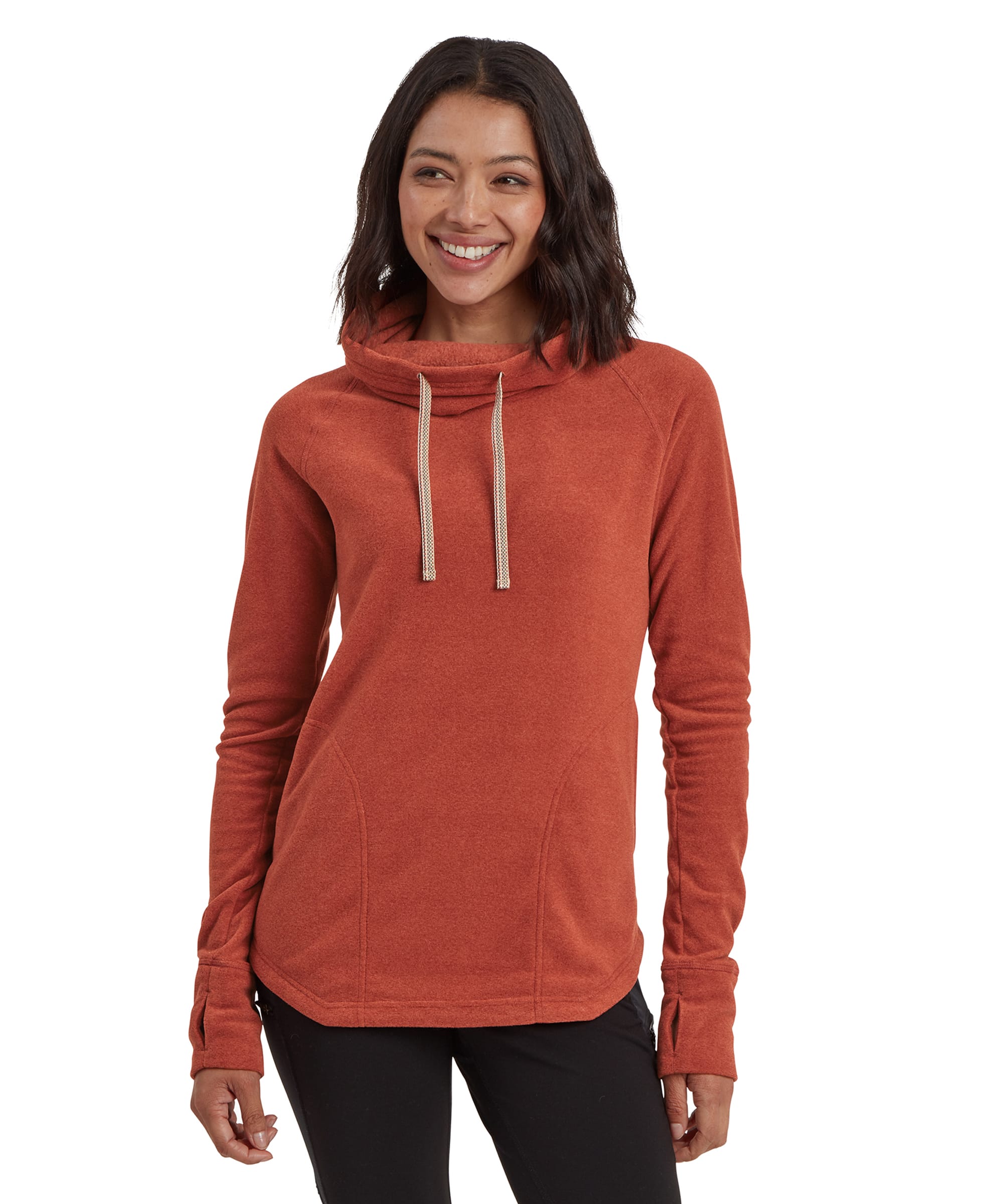 A woman wearing a warm, Sherpa Adventure Gear Rolpa Eco Pullover in Brown with a high, adjustable cowl neck featuring drawstrings. The pullover has a rounded hem and is paired with black leggings. The model smiles confidently, standing in a relaxed pose.