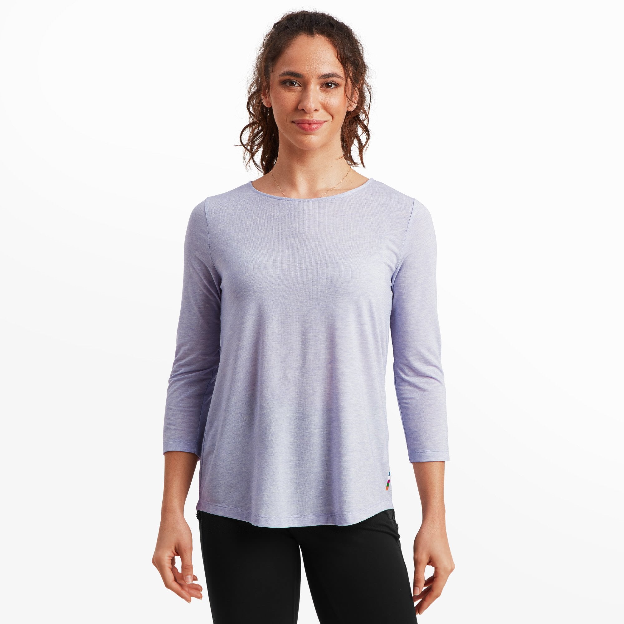 A woman wearing a Sherpa Adventure Gear Asha 3/4 Sleeve Top in Purple, smiling directly at the camera. The top has a relaxed fit with a round neckline and a smooth texture, paired with black pants.