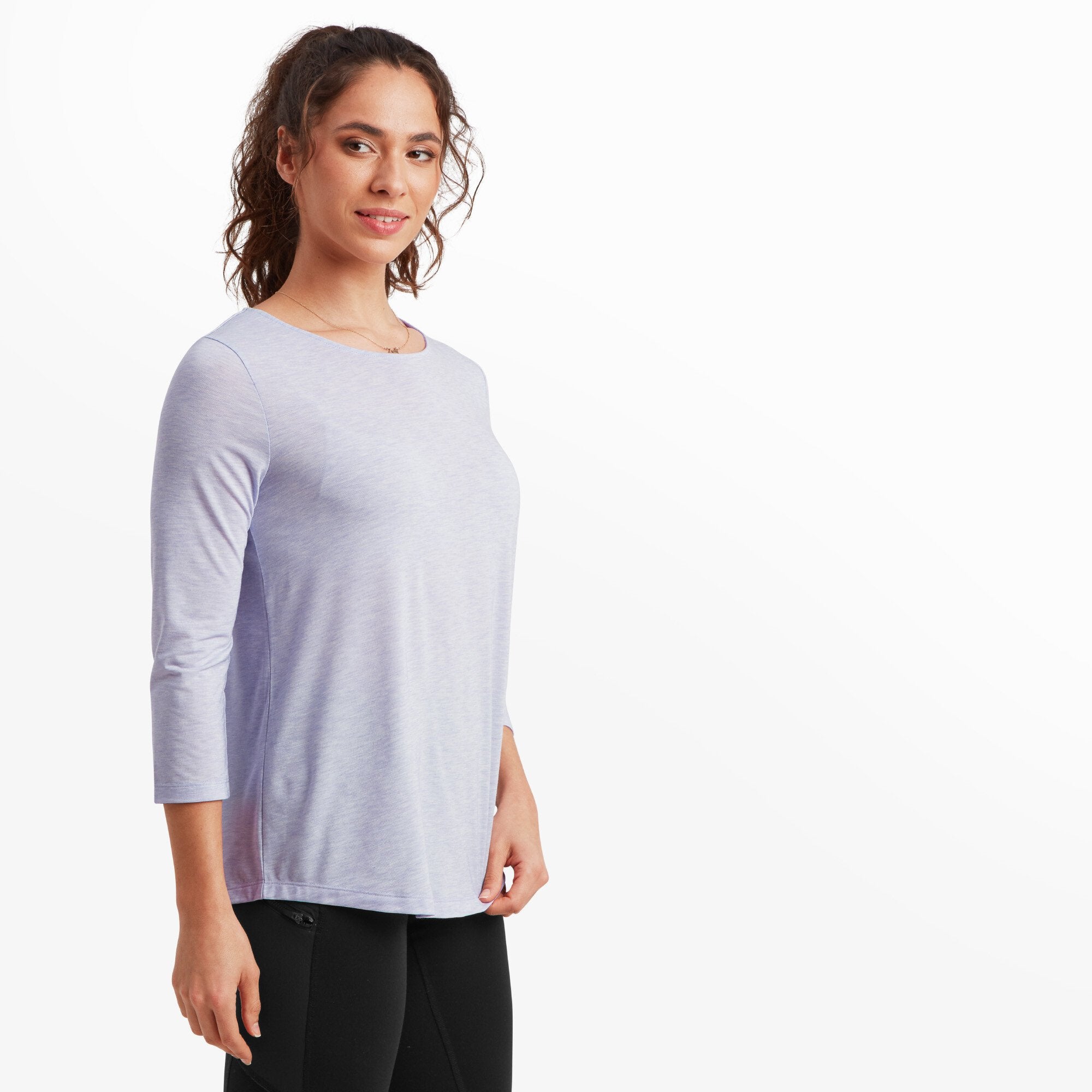 The same woman turned slightly to her left, showing the side profile of the Sherpa Adventure Gear Asha 3/4 Sleeve Top in Purple. The top's hem is slightly rounded and falls loosely over her hip, enhancing the casual yet elegant look.