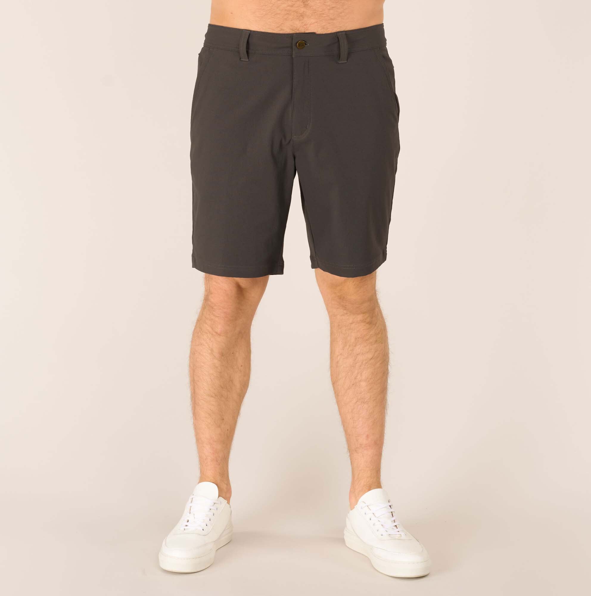 A straight-on front view of a man wearing Sherpa Adventure Gear Bara Shorts in Grey, showcasing their tailored fit and mid-thigh length. The shorts feature a button closure at the waistband and a clean design with subtle stitching. The model is wearing white trainers, highlighting the casual style of the shorts.