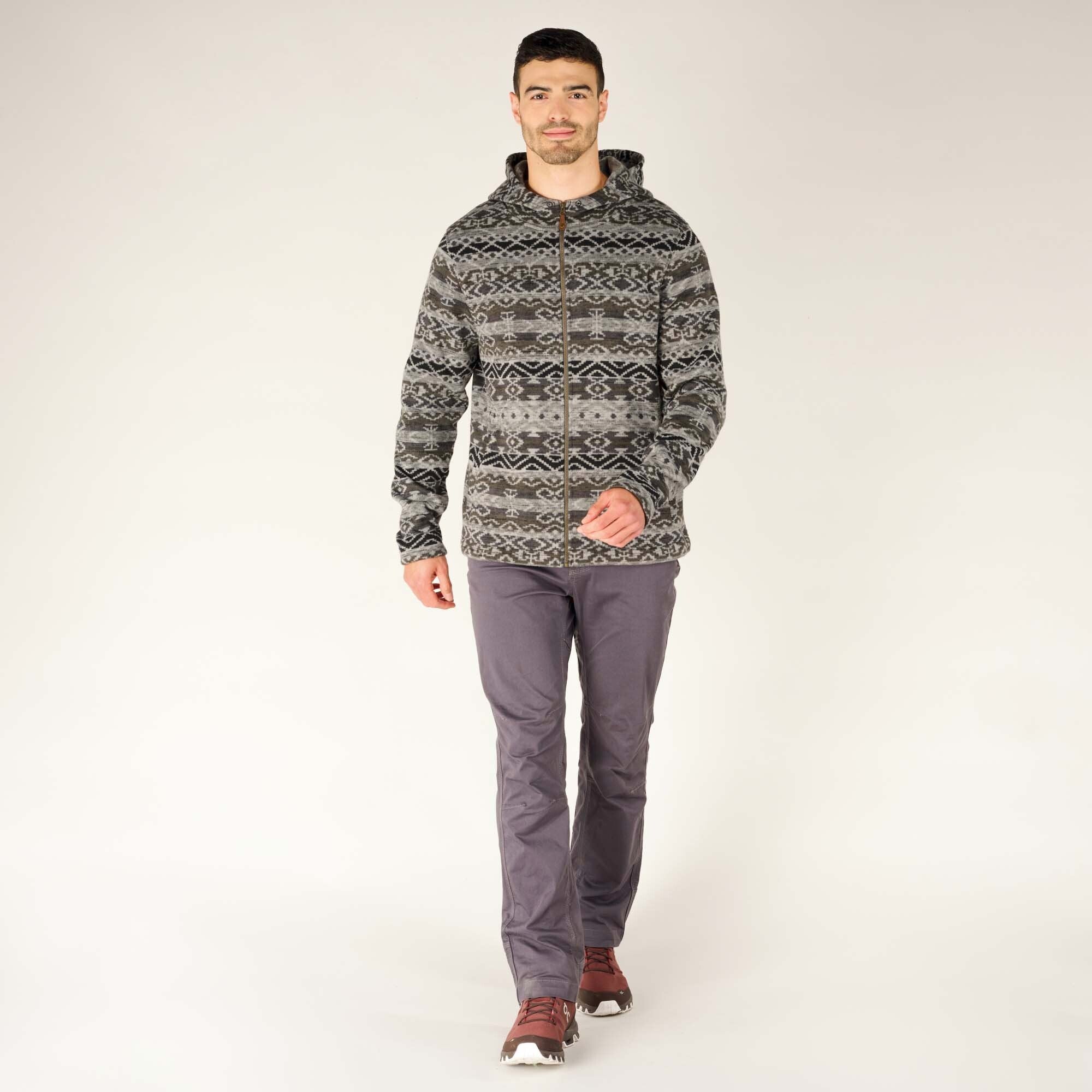 The model is standing in a relaxed pose, showcasing the full length of the Sherpa Adventure Gear Bhutan Full Zip Hoodie in Grey paired with grey pants and brown hiking shoes. The hoodie has a symmetrical black and white pattern that runs across the chest and sleeves.