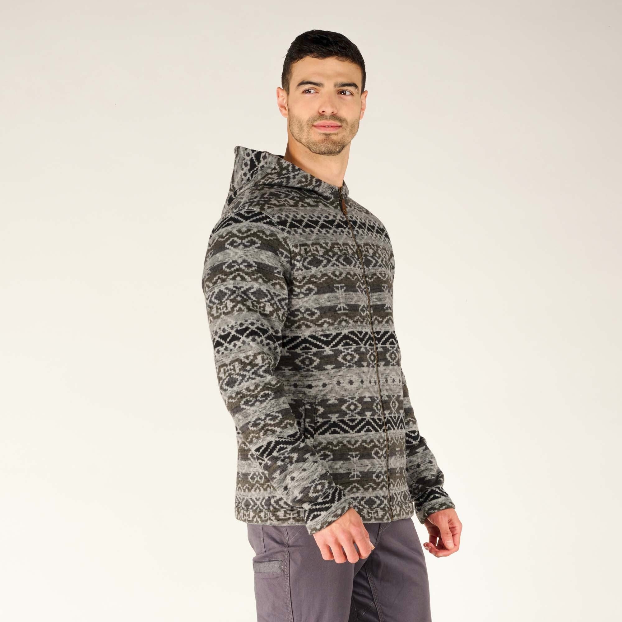 The model is turned slightly to his left, giving a side angle of the Sherpa Adventure Gear Bhutan Full Zip Hoodie in Grey. The hood is up, revealing its patterned design. The fit appears slightly relaxed, with the sleeves extending just past the wrists.