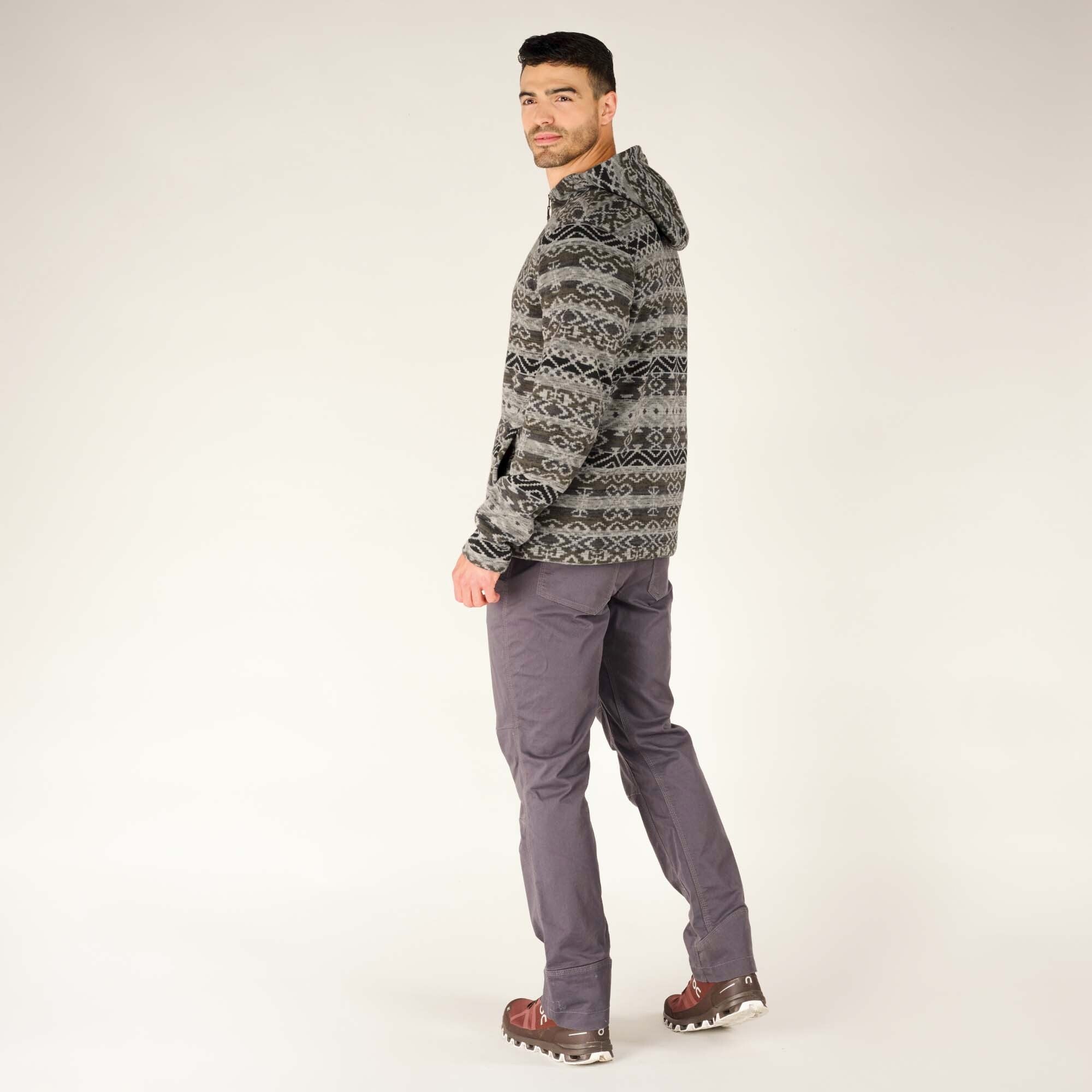 The model is slightly turned away, giving a three-quarter rear view of the Sherpa Adventure Gear Bhutan Full Zip Hoodie in Grey. The detailed pattern wraps around the entire garment, and the relaxed hood drapes naturally on his back.