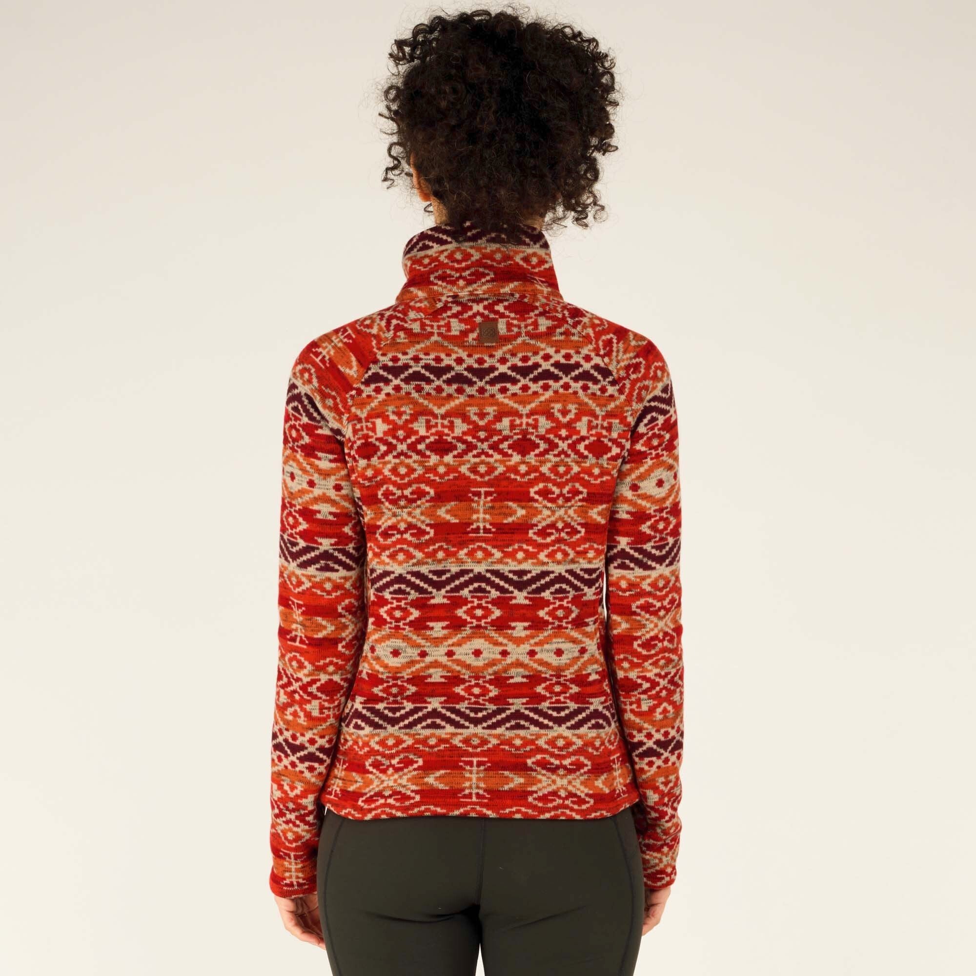 A back view of the model wearing the same Sherpa Adventure Gear Bhutan Pullover in Red, displaying the full geometric design across the back. The high collar stands up, and the pullover fits comfortably over her black leggings. The long sleeves extend just past her wrists, showing a cozy fit.