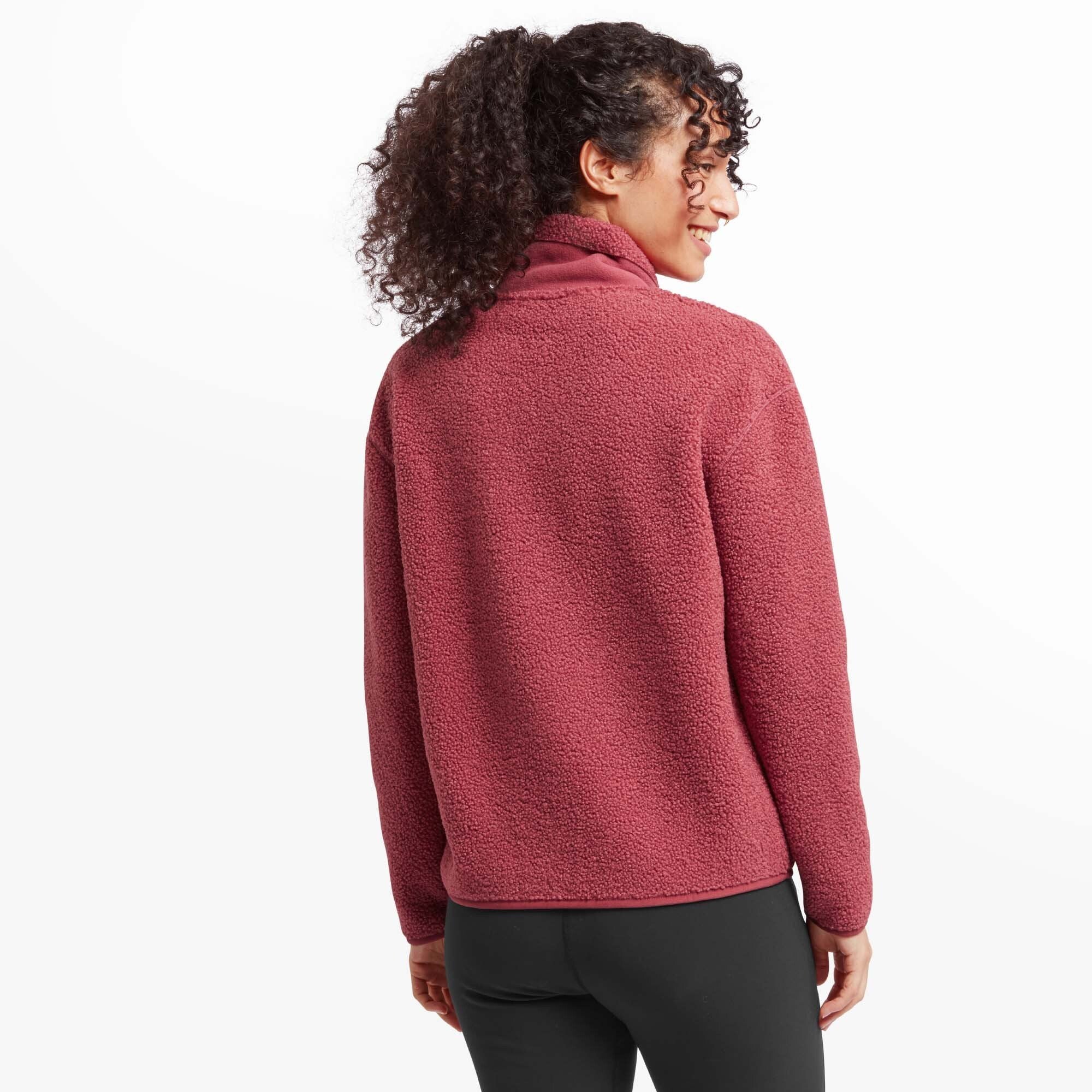 A rear view of the woman wearing the Sherpa Adventure Gear Chamlang Half Zip Pullover in Red. The back of the pullover is visible, displaying its smooth and seamless design, with the fleece texture extending uniformly across.