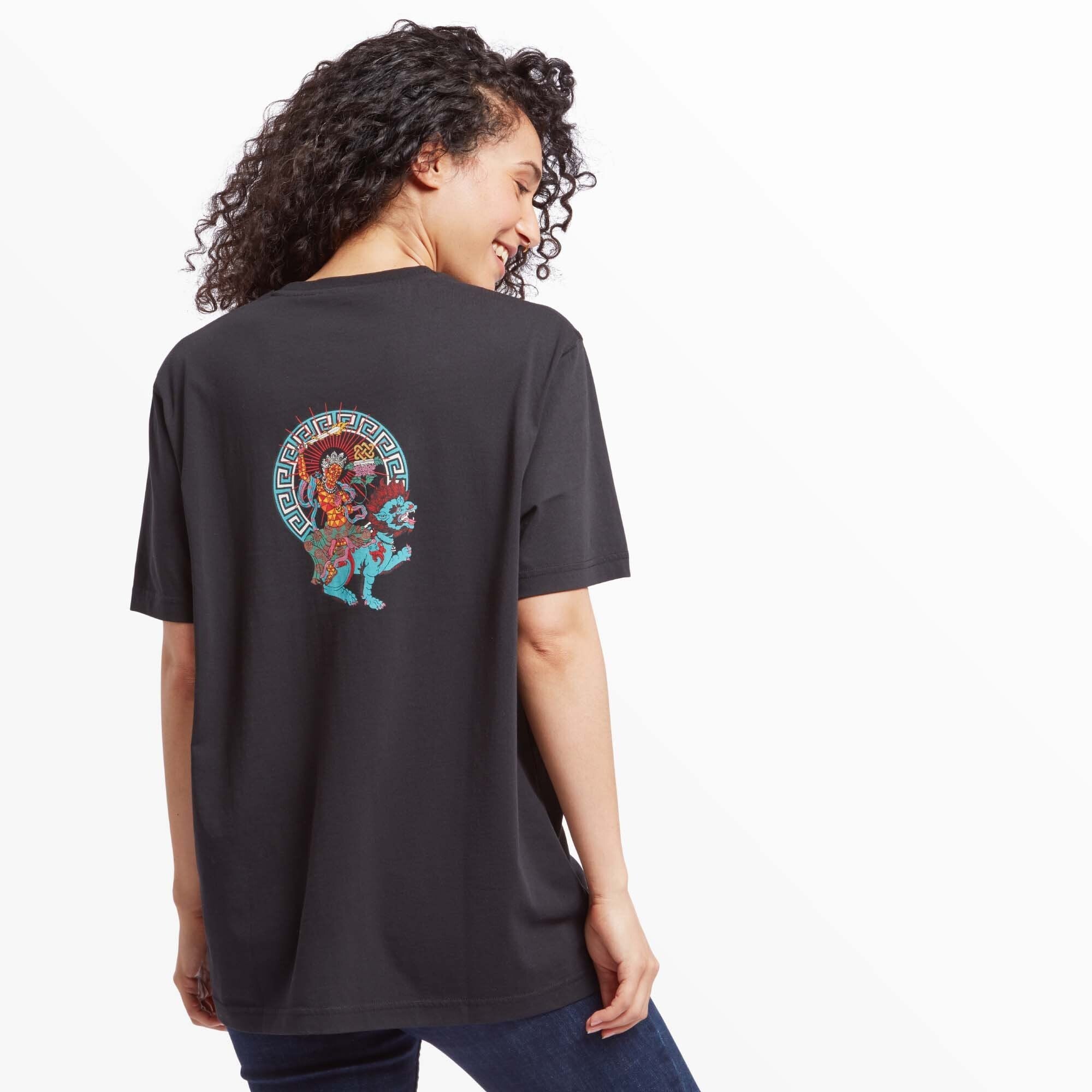 A woman showcasing the back of the Sherpa Adventure Gear Deity T-Shirt in Black. The large, colorful deity design is fully visible, adding vibrancy and uniqueness to the shirt. She pairs the shirt with dark jeans, maintaining a casual style.