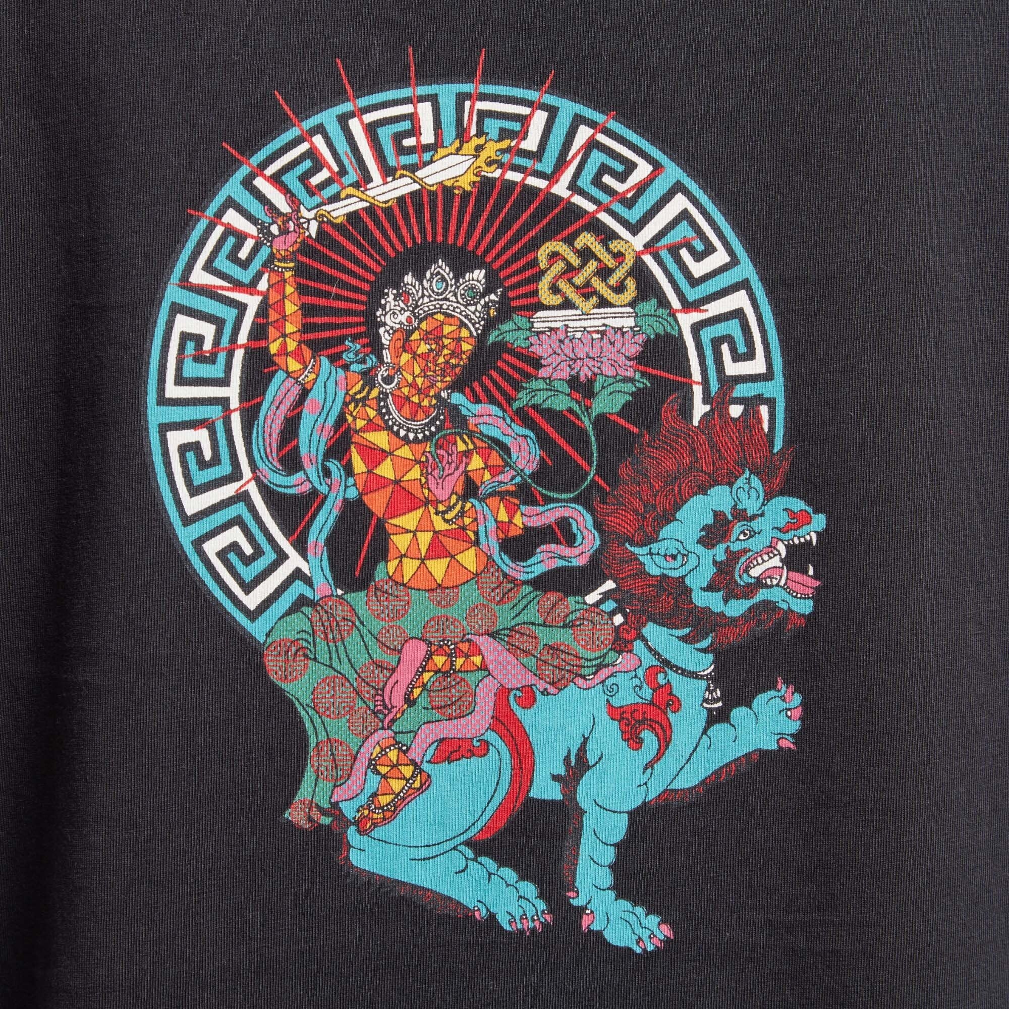 A detailed close-up of the deity graphic on the back of the Sherpa Adventure Gear Deity T-Shirt in Black. The vibrant colors of the deity seated on a blue lion, surrounded by intricate patterns, are clearly displayed. The design highlights the artistry and cultural inspiration behind the shirt.