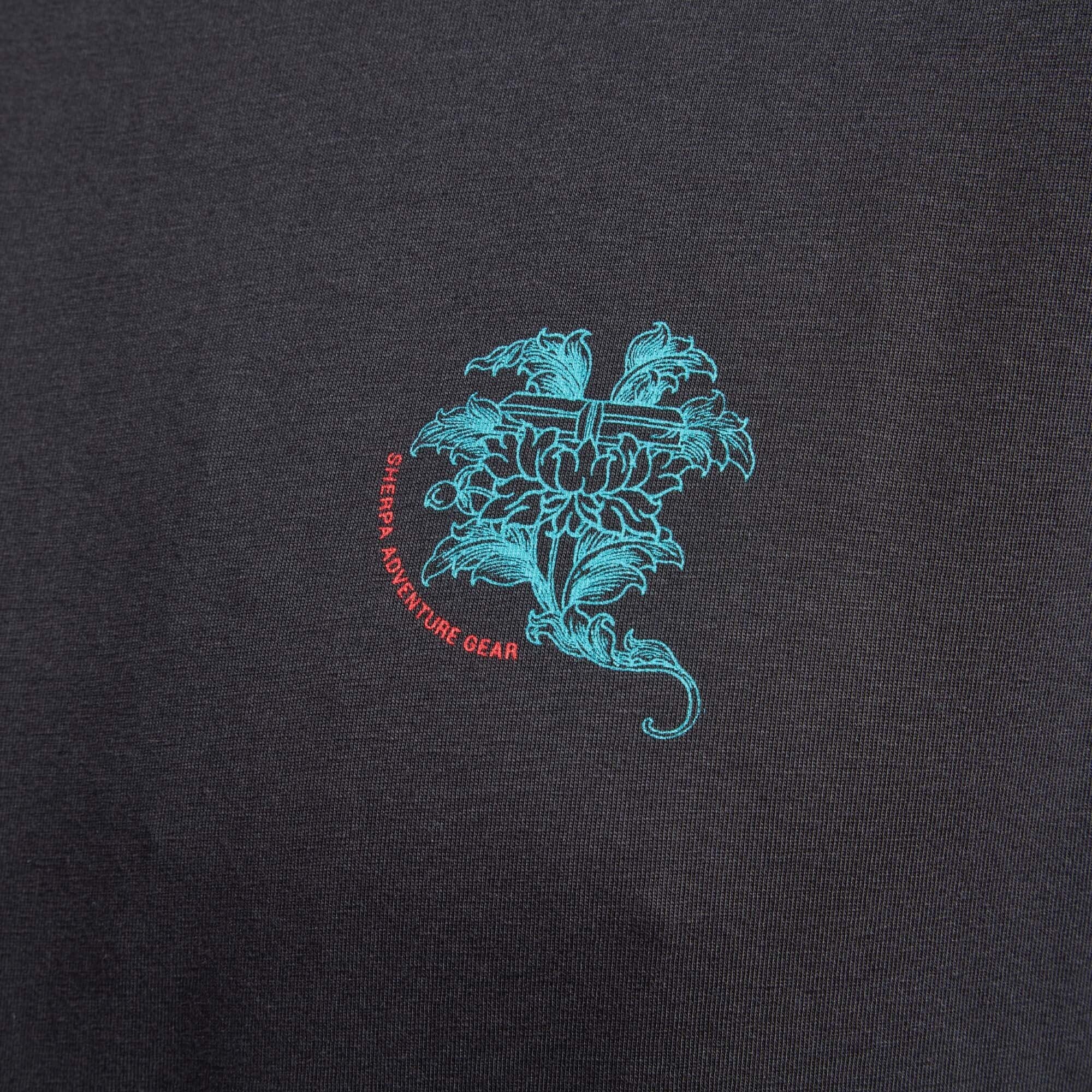 A close-up of the small lotus flower graphic on the chest of the Sherpa Adventure Gear Deity T-Shirt in Black. The intricate design is in turquoise and red, with the Sherpa Adventure Gear logo encircling the flower.