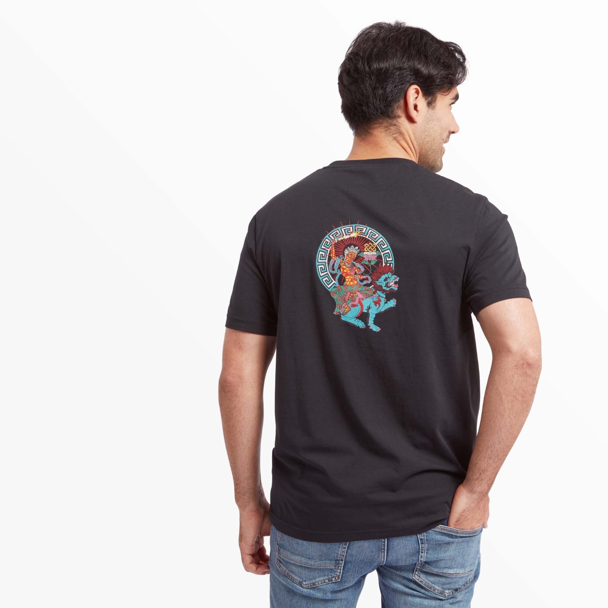 A man modeling the back of the Sherpa Adventure Gear Deity T-Shirt in Black. The back features a large, colorful deity design of a figure seated on a blue lion, surrounded by intricate geometric patterns. The bold colors and intricate details stand out against the black fabric.