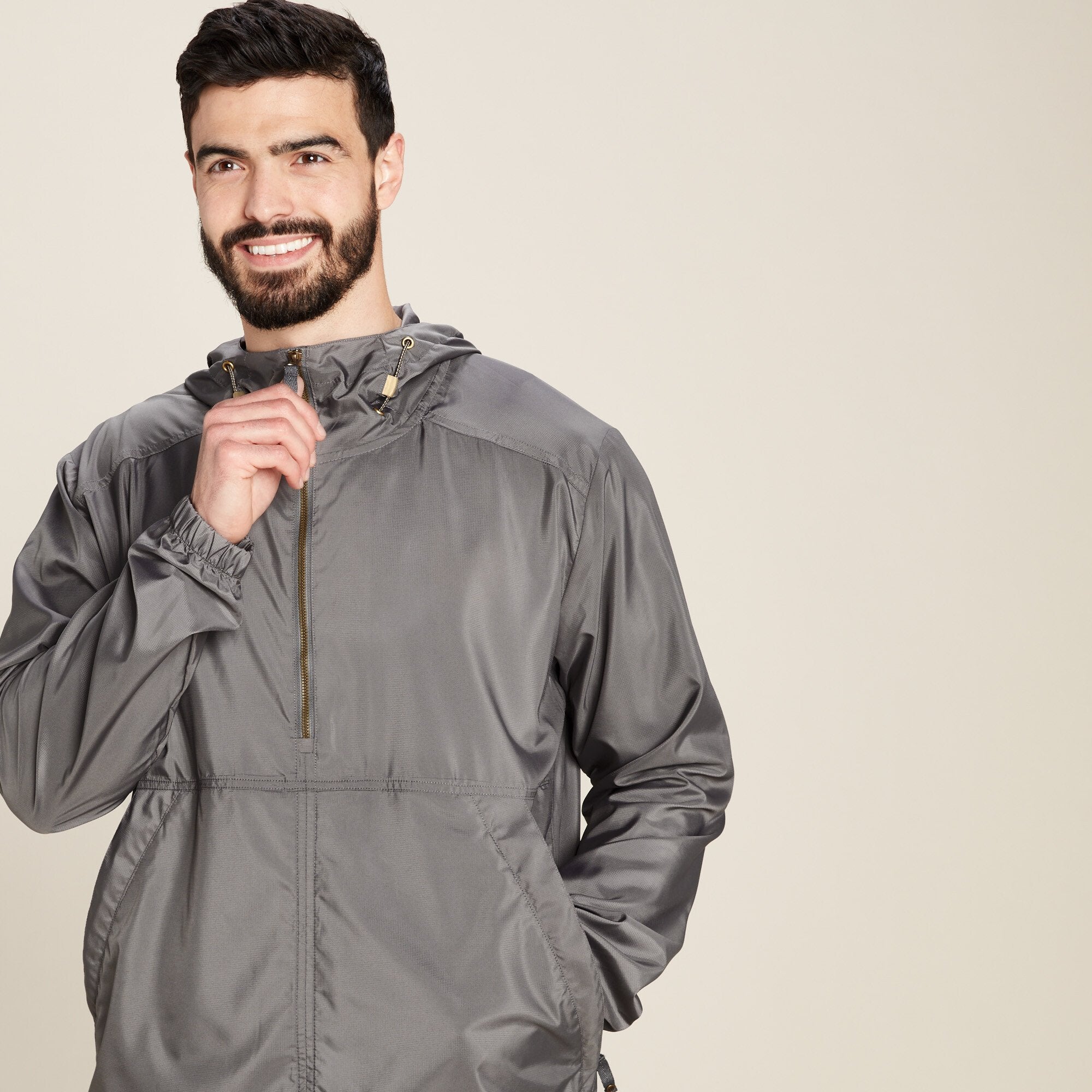 A side-angle view of the same man wearing the Sherpa Adventure Gear Halka Anorak Jacket in Grey. The man has one hand raised, holding the zipper, as if preparing to zip the jacket up. This showcases the functional zipper detail and highlights the smooth finish of the fabric.