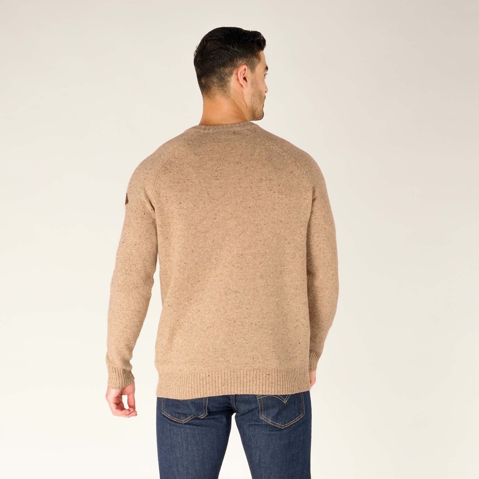 A rear view of the male model showcasing the back of the Sherpa Adventure Gear Kangtega Crew Sweater in Beige. The ribbed hem and shoulder seams are visible, along with a relaxed fit. He continues to wear dark blue jeans.