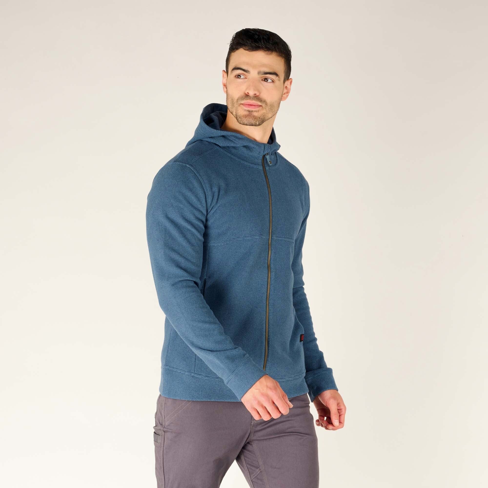 A side profile of the man wearing the Sherpa Adventure Gear Kula Full Zip Hoodie in Blue. His relaxed pose emphasises the tailored fit of the hoodie and its comfortable style.