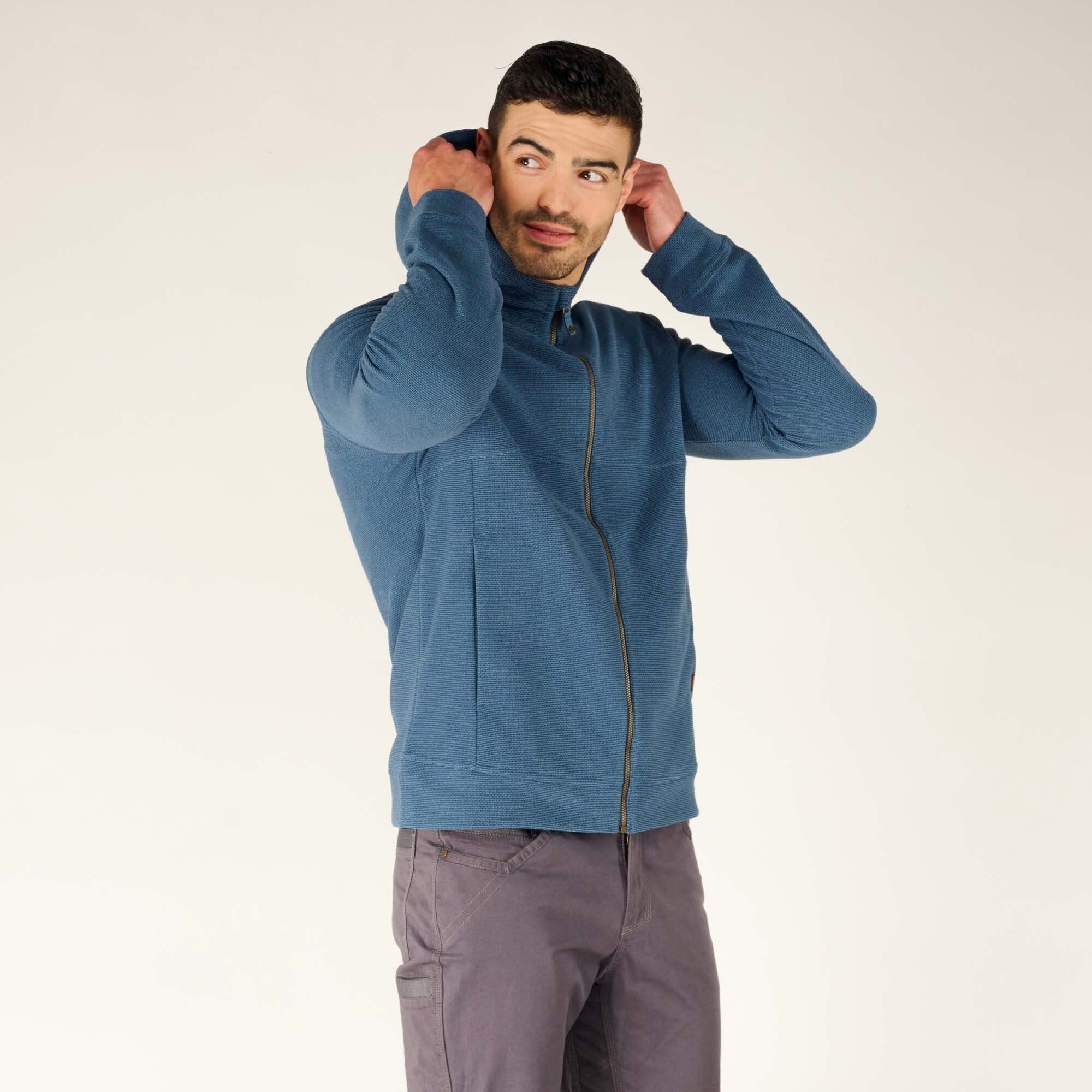 The man wearing the Sherpa Adventure Gear Kula Full Zip Hoodie in Blue with the hood fully up, walking confidently towards the camera. This showcases the hood’s snug fit and the overall practicality of the garment.