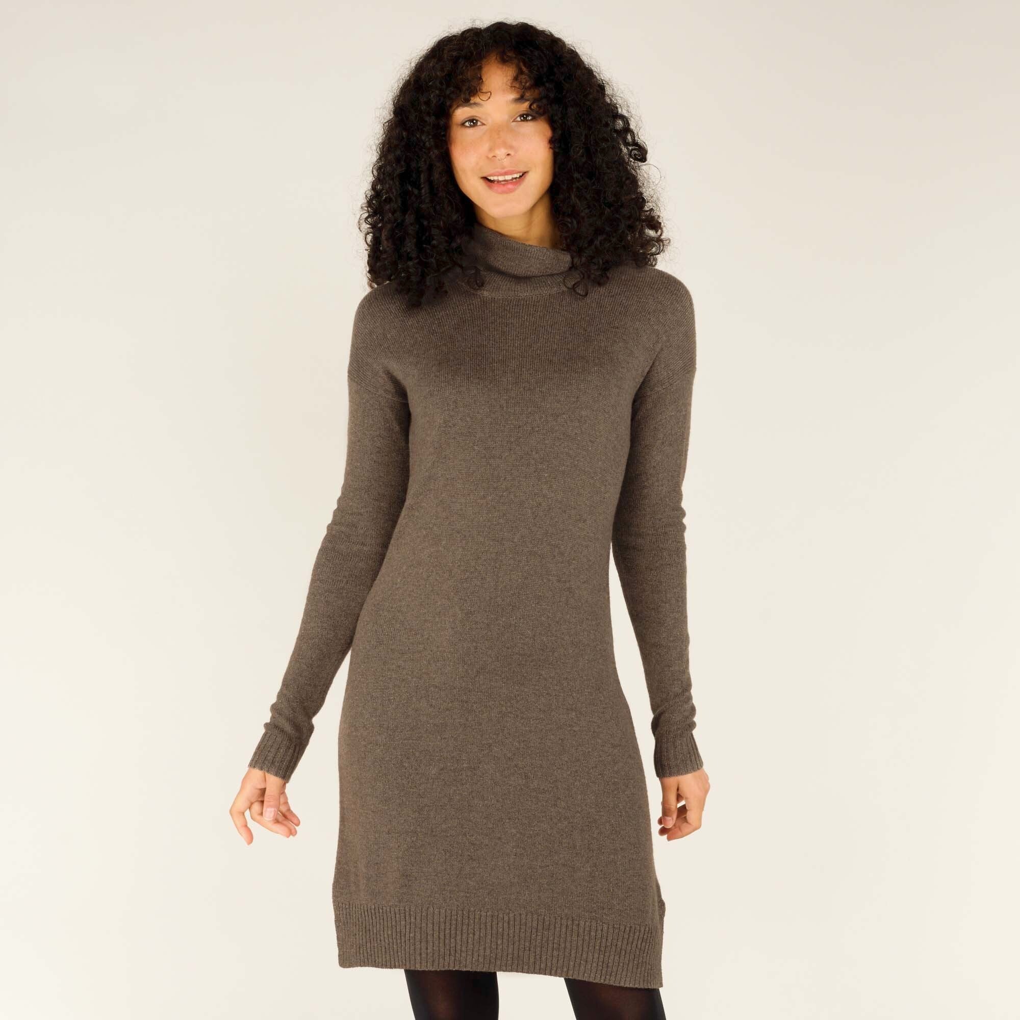 A woman models a Sherpa Adventure Gear Lhakpa Mock Neck Dress in Grey with a fitted silhouette. The hemline falls just above the knee, and the design includes ribbed cuffs and hem. She stands facing forward, smiling slightly, highlighting the simple elegance of the dress.