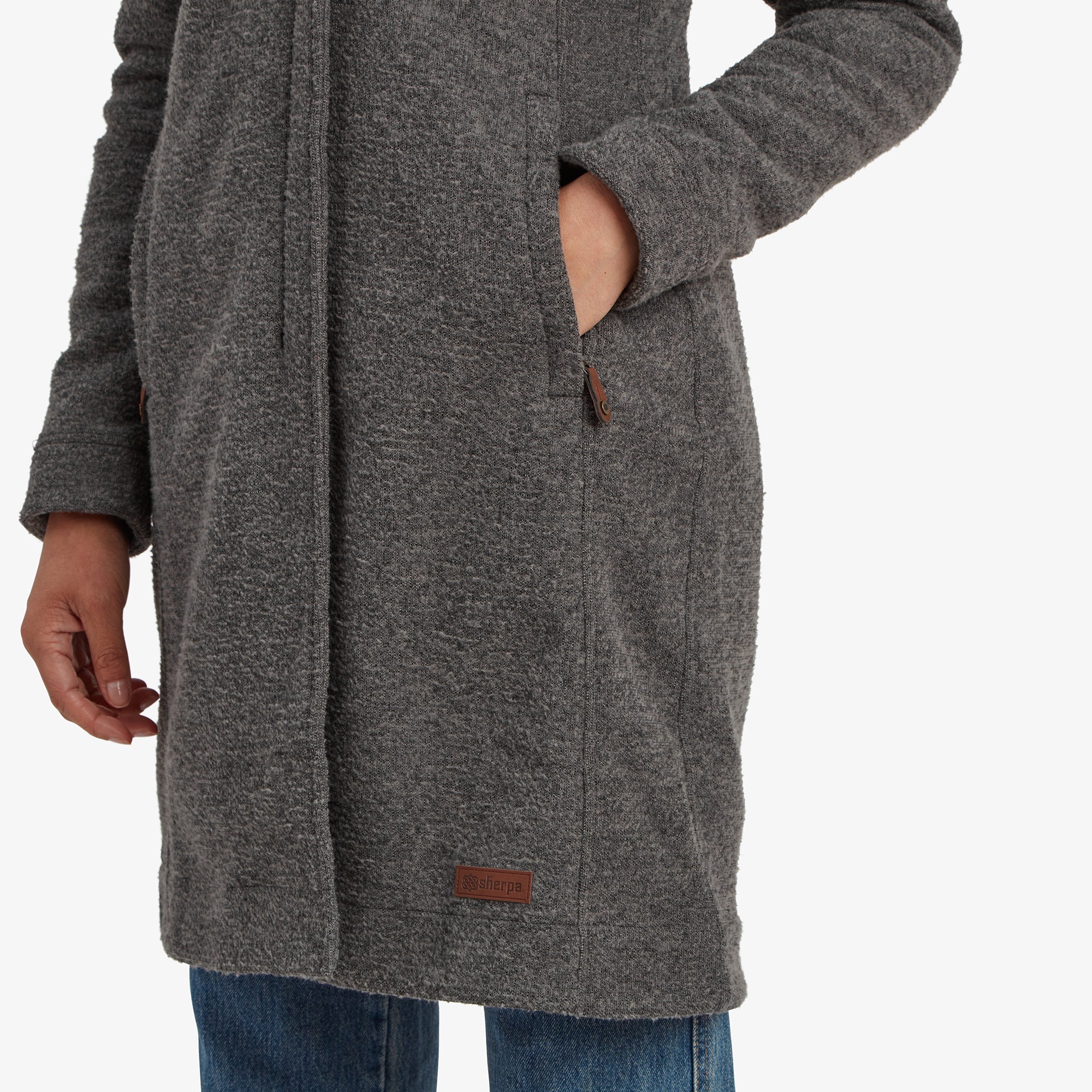 A zoomed-in view of the Sherpa Adventure Gear Lhamu Jacket in Grey’s high collar, featuring a single round button with an intricate carved design. The grey textured fabric appears thick and warm. A beige knitted sweater is visible underneath the coat.