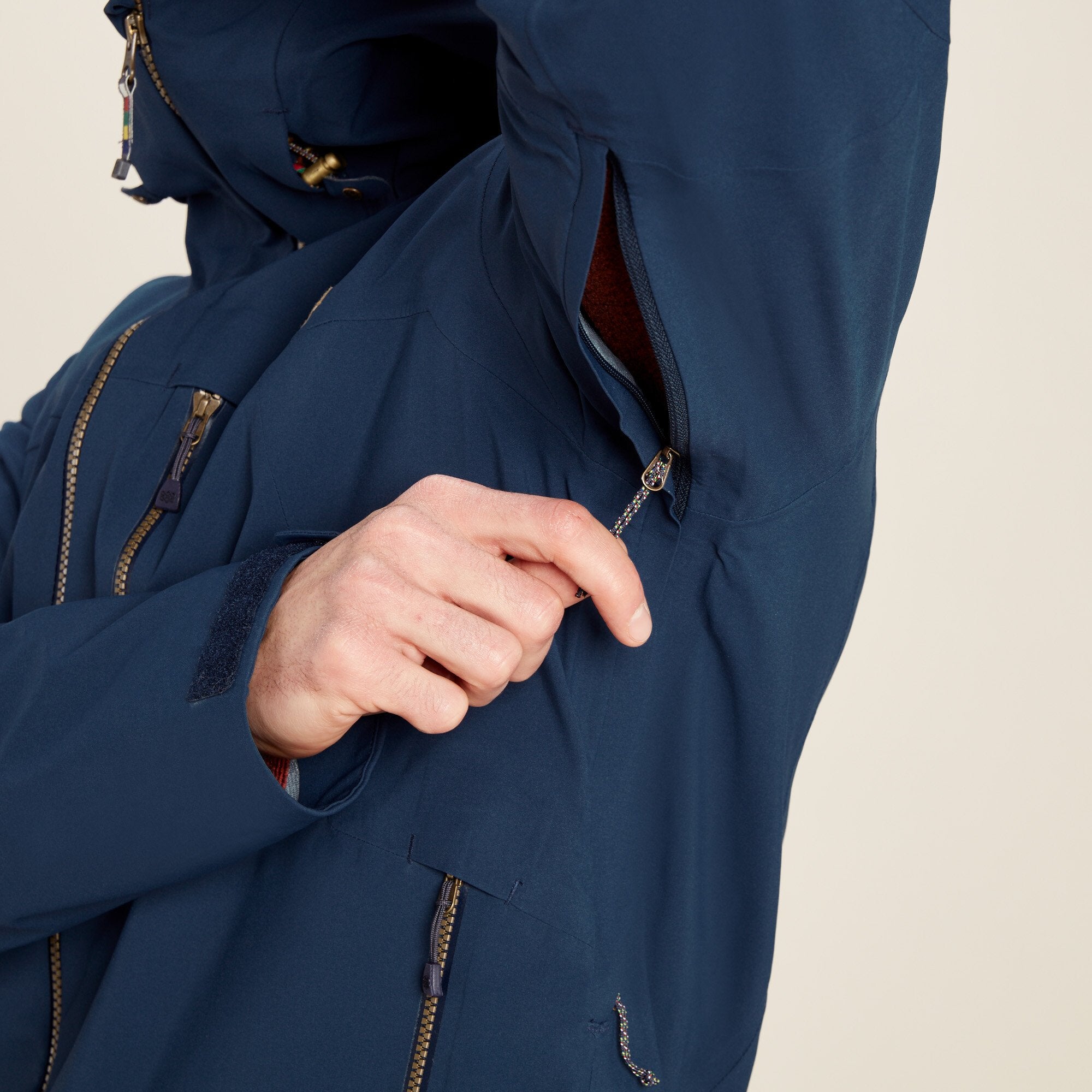 A man demonstrates the zippered underarm vent feature of the Sherpa Adventure Gear Makalu Jacket in Blue. He is pulling open the vent zipper located under the arm, revealing the inner breathable fabric of the jacket.