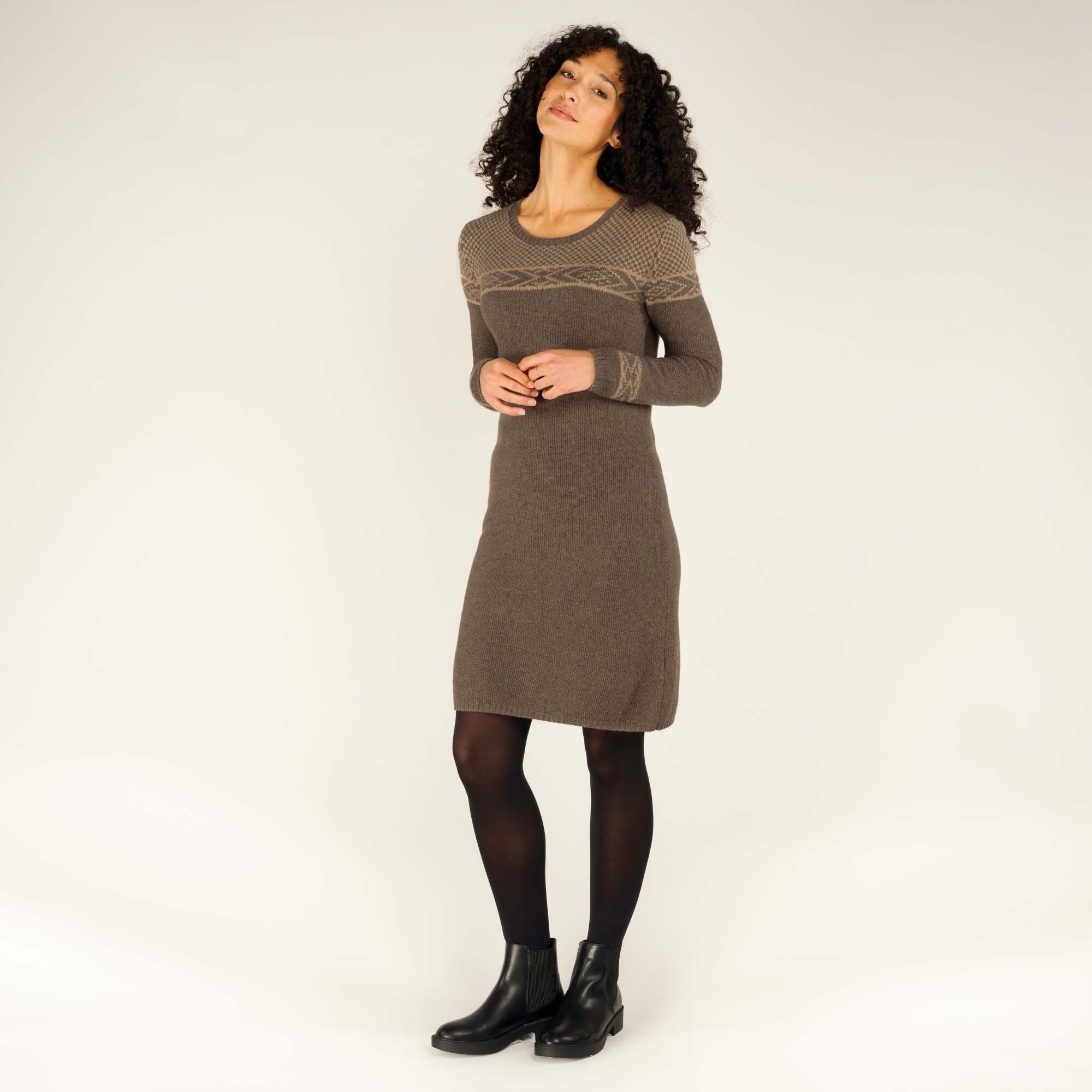 The same Sherpa Adventure Gear Maya Texture Dress in Grey is showcased in a full-frontal standing pose. The model's hands are clasped lightly, highlighting the dress's detailed knitwork on the upper chest and sleeves. She is styled with black tights and black ankle boots, adding a contemporary touch to the outfit.