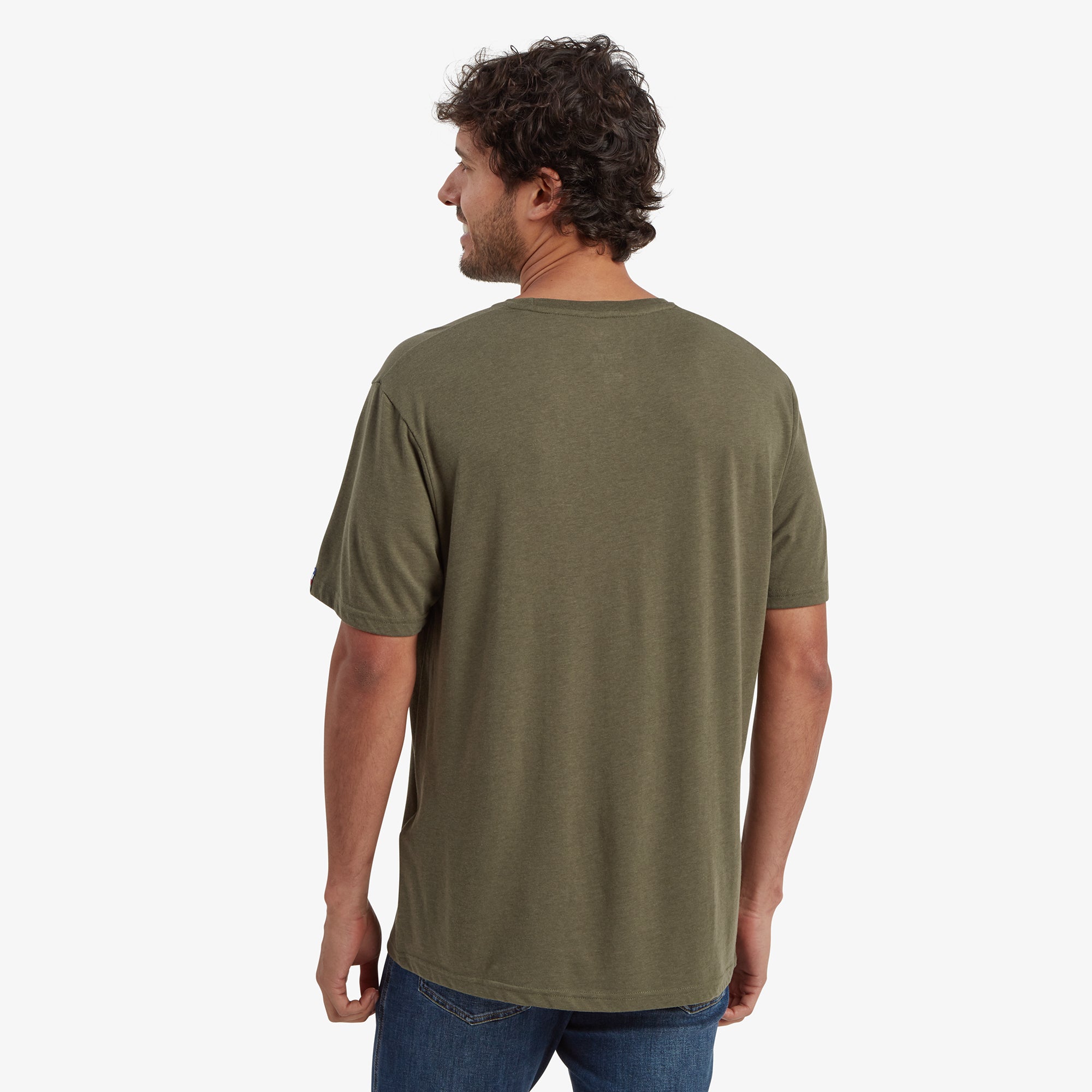 A rear view of the Sherpa Adventure Gear Bali T-Shirt in Green worn by the male model. The t-shirt’s plain design continues across the back, with a seamless cut for a clean and minimalistic appearance. The model’s posture highlights the casual fit of the shirt.