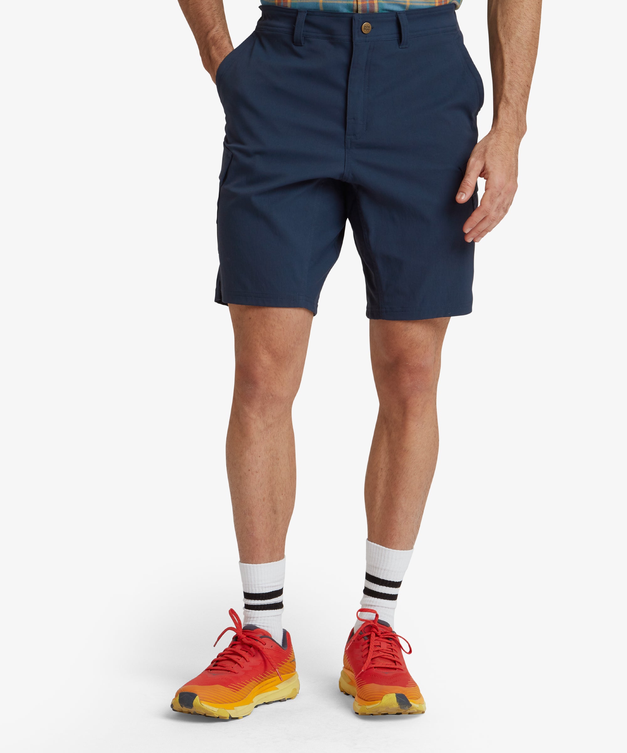 A close-up front view of a man wearing Sherpa Adventure Gear Bara Cargo Shorts in Blue. The shorts feature a simple, clean design with a button closure and pockets on both sides. The material appears lightweight and suitable for outdoor activities.