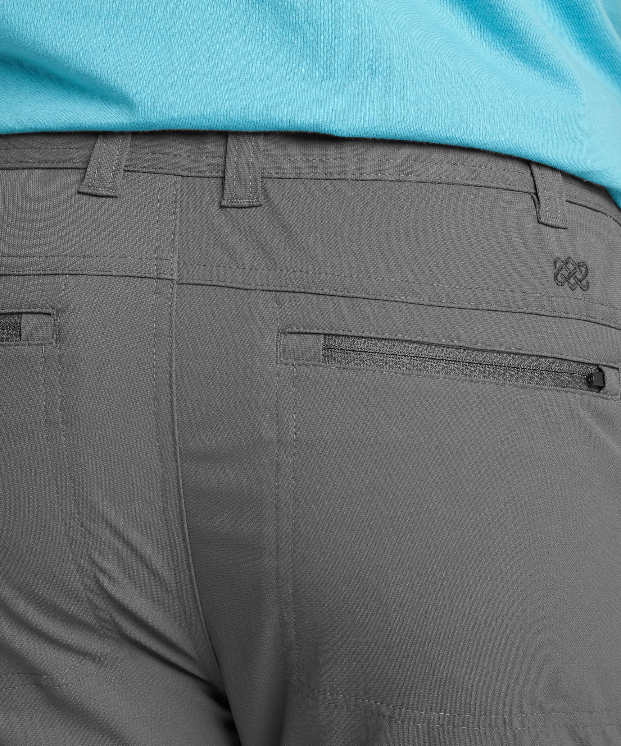 A close-up of the lower side pocket on the Sherpa Adventure Gear Bara trousers in Grey, with a hand pulling the zipper to demonstrate secure storage. The trousers' rugged yet refined fabric and zipper detail highlight their outdoor-friendly design.