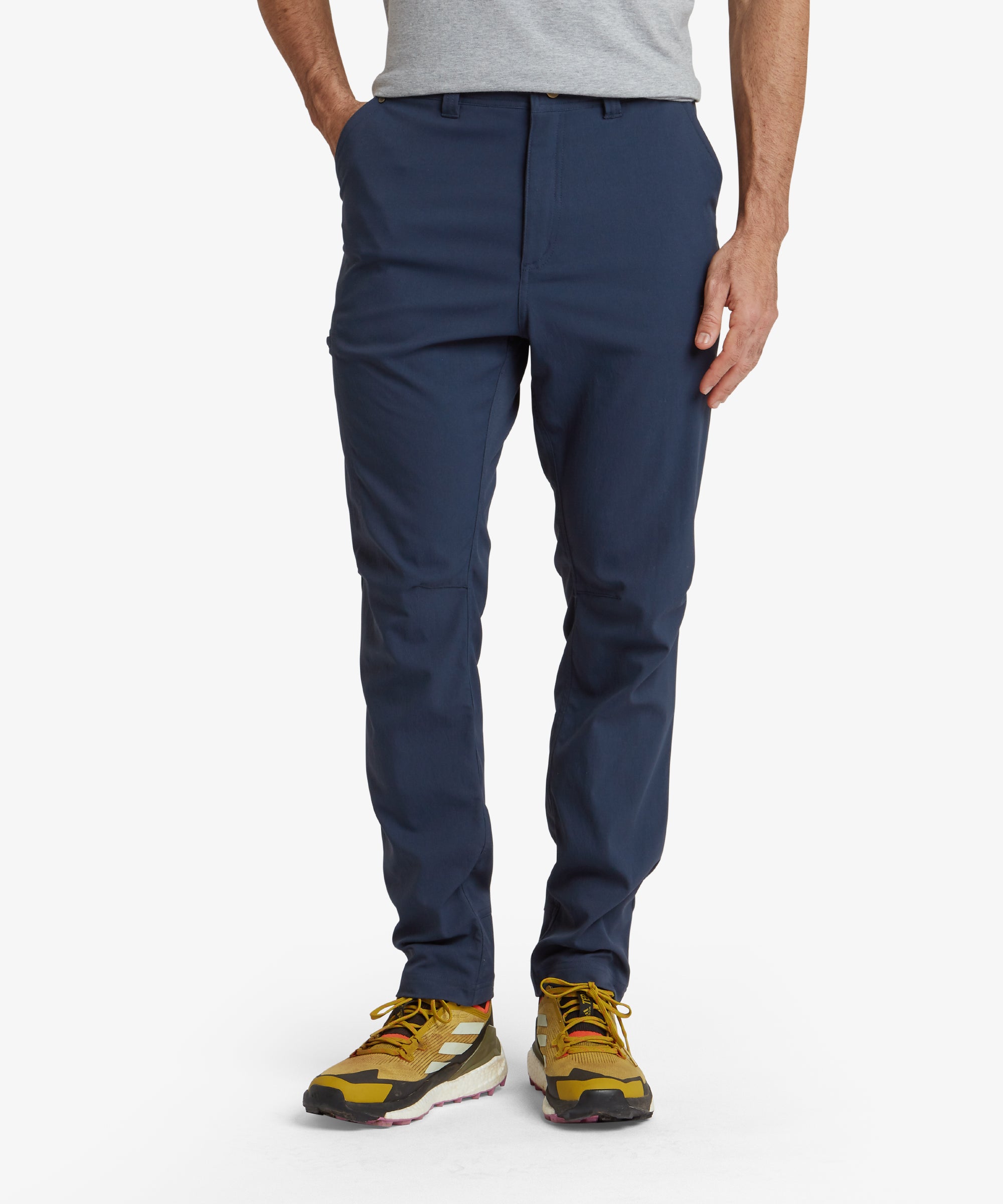 Close-up view of a male model wearing Sherpa Adventure Gear Bara trousers in Blue. The trousers feature a tailored fit with a button closure and visible front pockets, emphasising the clean and sleek design. The stitching detail along the seams enhances the minimalist aesthetic of the trousers.