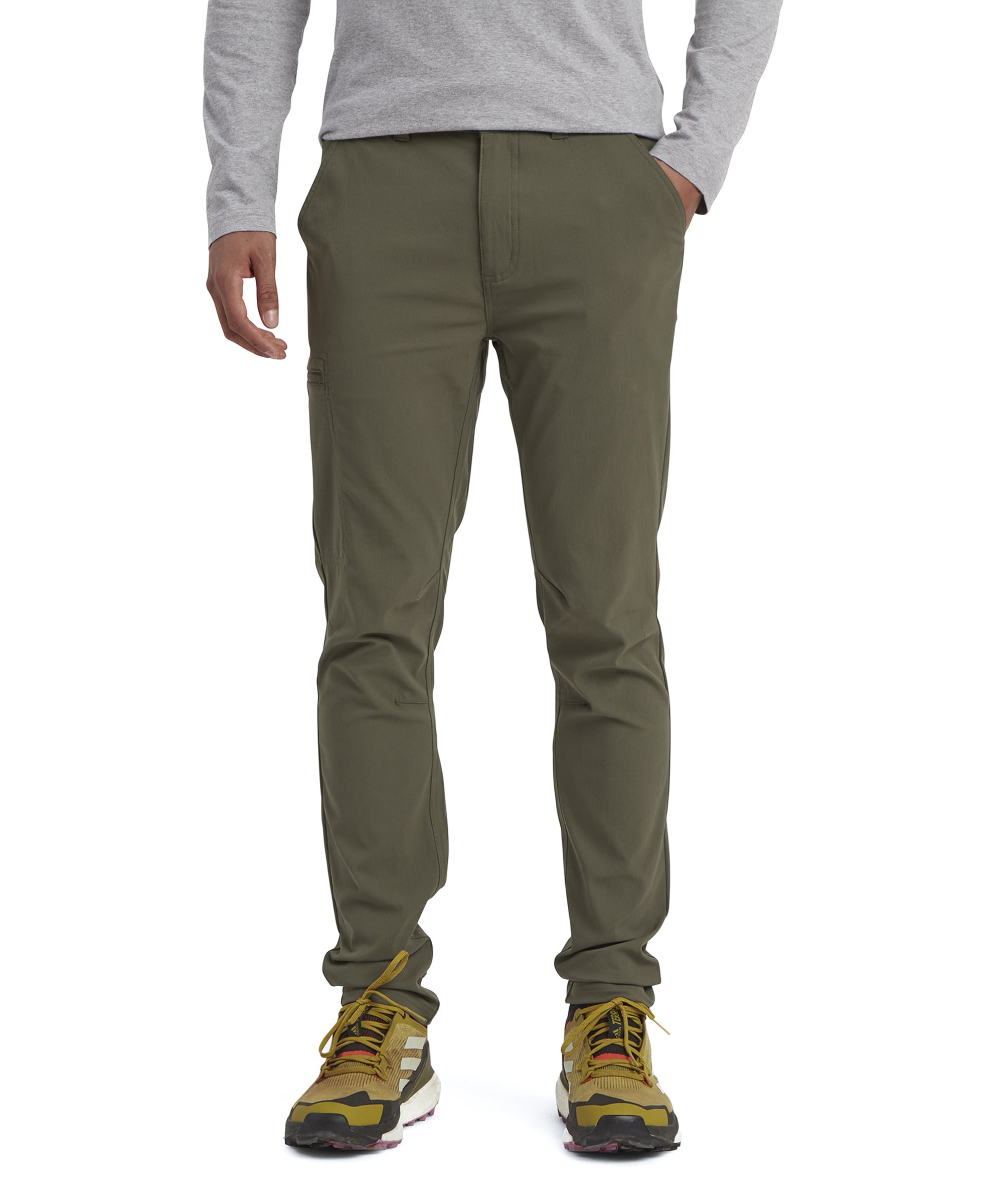 A model wearing slim-fit Sherpa Adventure Gear Bara trousers in Green with a straight leg design. The trousers feature front pockets and are paired with a gray long-sleeve shirt and yellow hiking trainers.