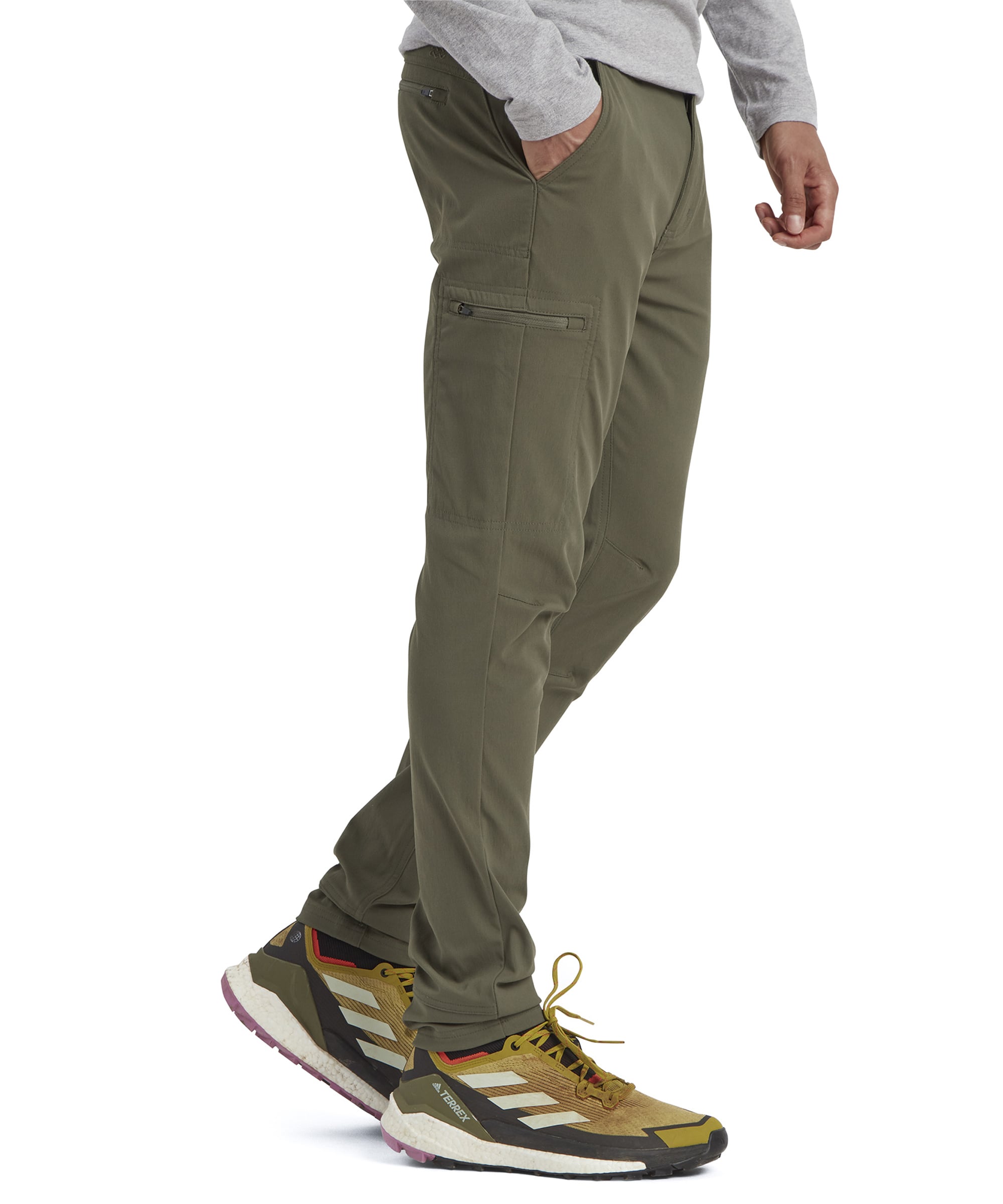 A profile view showing the Sherpa Adventure Gear Bara trousers in Green' side pocket detail, zippered compartments, and clean stitching. The model's stance highlights the tailored fit and practicality of the trousers.