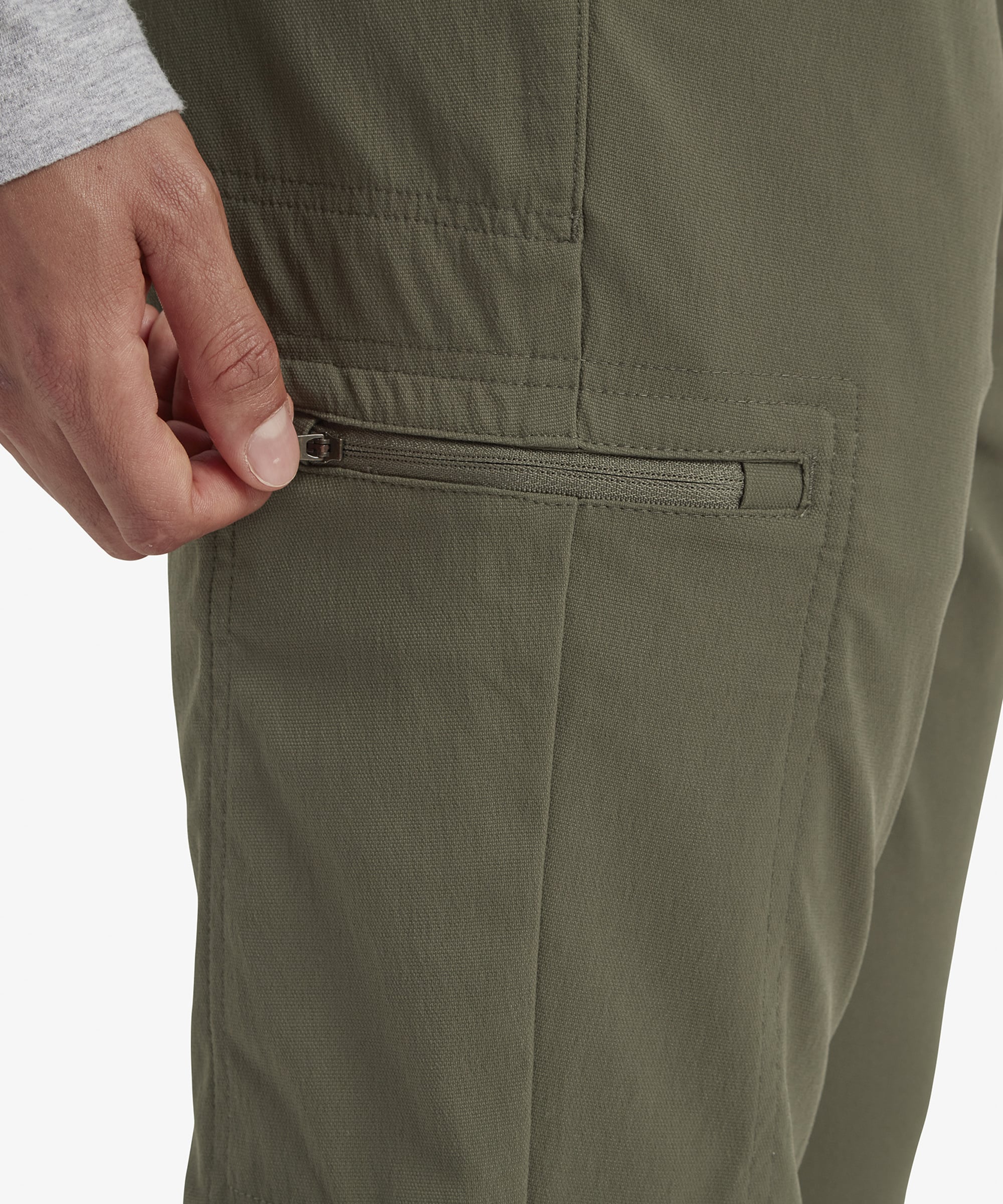 A detailed close-up of the zippered side pocket of the Sherpa Adventure Gear Bara trousers in Green, showing its functional design, sleek finish, and practicality for outdoor activities.