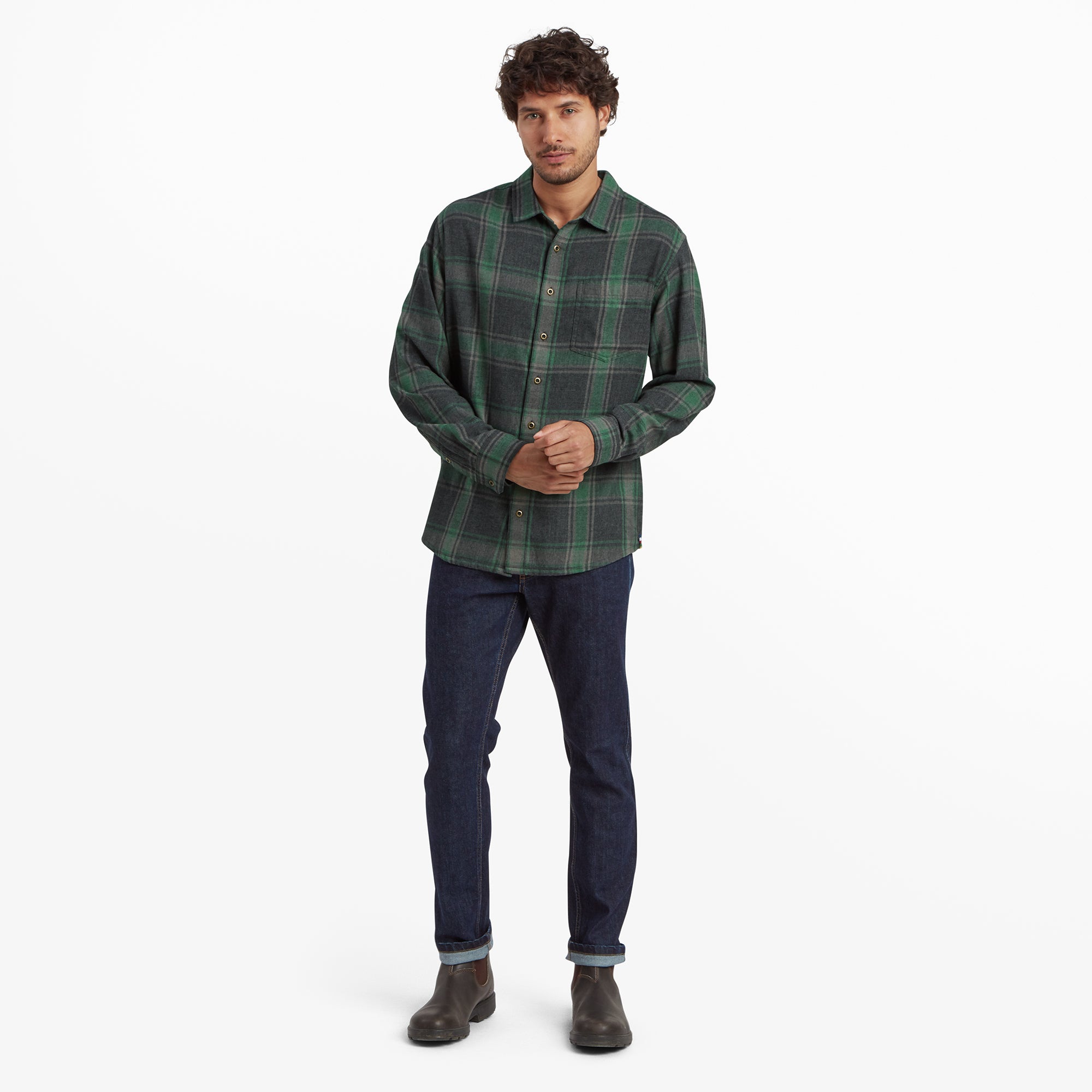 The same man dressed in the Sherpa Adventure Gear Batsa Long Sleeve Shirt in Black, standing in a full-body pose with dark blue jeans and brown boots. He stands confidently with his hands clasped in front of him, presenting a relaxed yet stylish look.