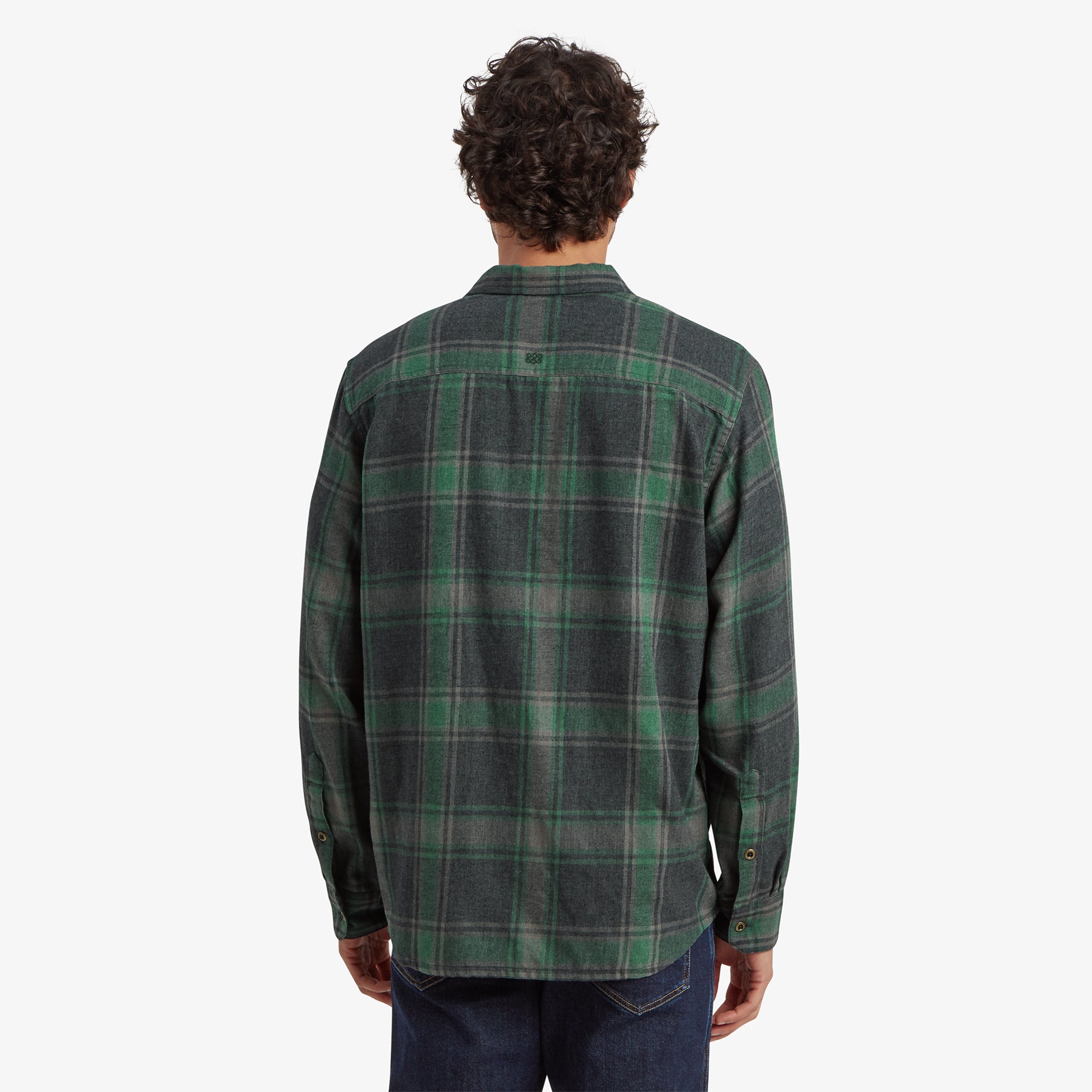 Back view of the Sherpa Adventure Gear Batsa Long Sleeve Shirt in Black, showing the shirt’s fit and its evenly spaced plaid pattern. The model pairs the shirt with dark blue jeans, standing straight with his arms relaxed.