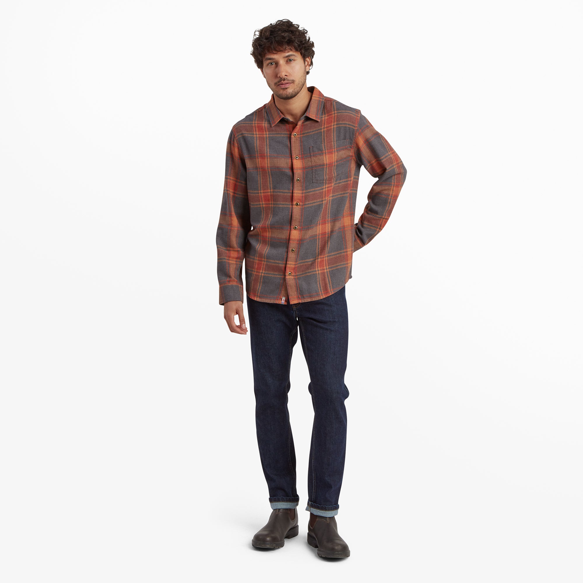 The same model is wearing the Sherpa Adventure Gear Batsa Long Sleeve Shirt in Red paired with dark jeans and brown boots. He is standing in a relaxed pose, highlighting the shirt's versatile style suitable for casual wear.