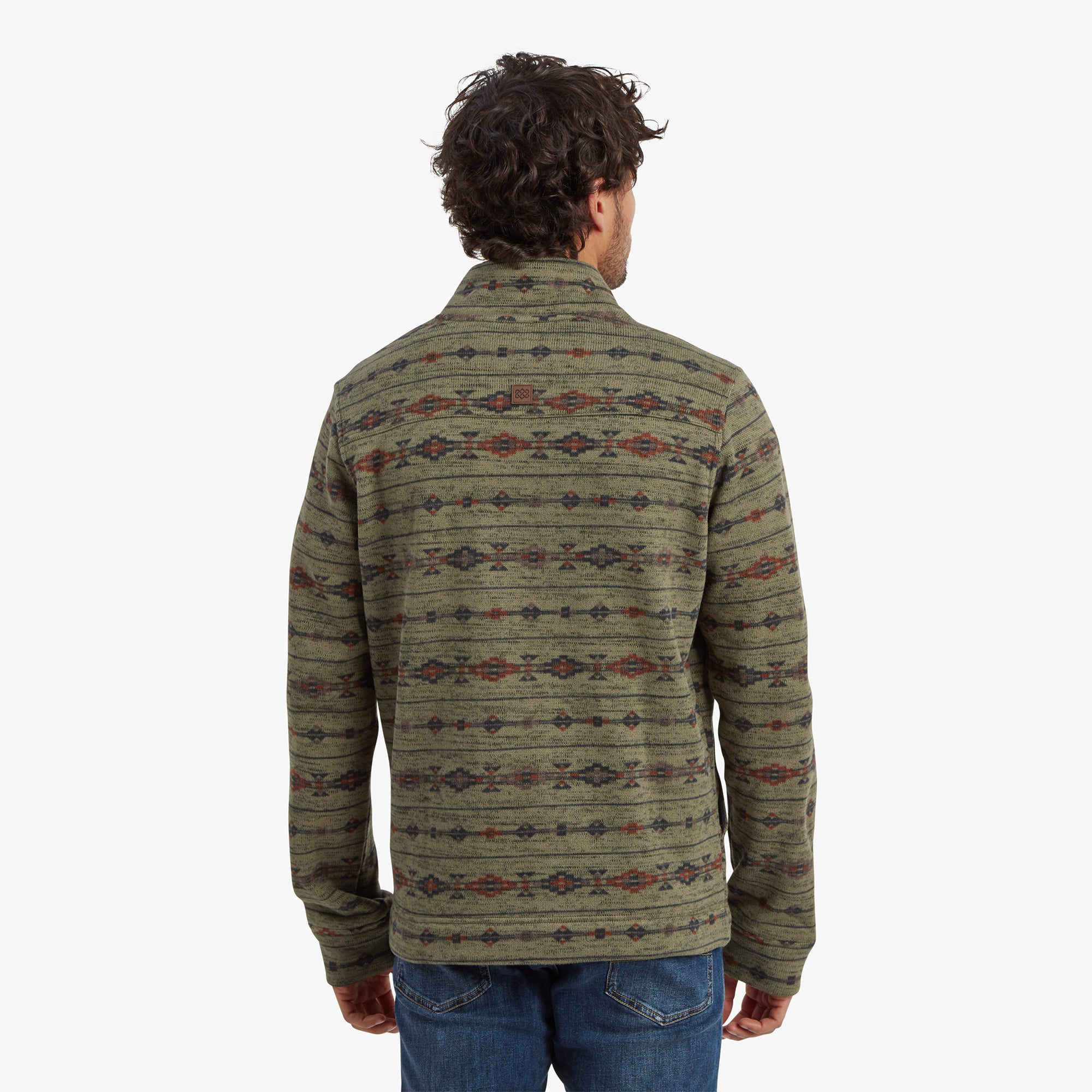 A clear view of the back of the Sherpa Adventure Gear Bhutan Full Zip Jacket in Green, displaying the intricate ethnic-inspired pattern running uniformly across the jacket. The high collar and clean stitching are prominent, complementing the casual blue jeans worn by the model.