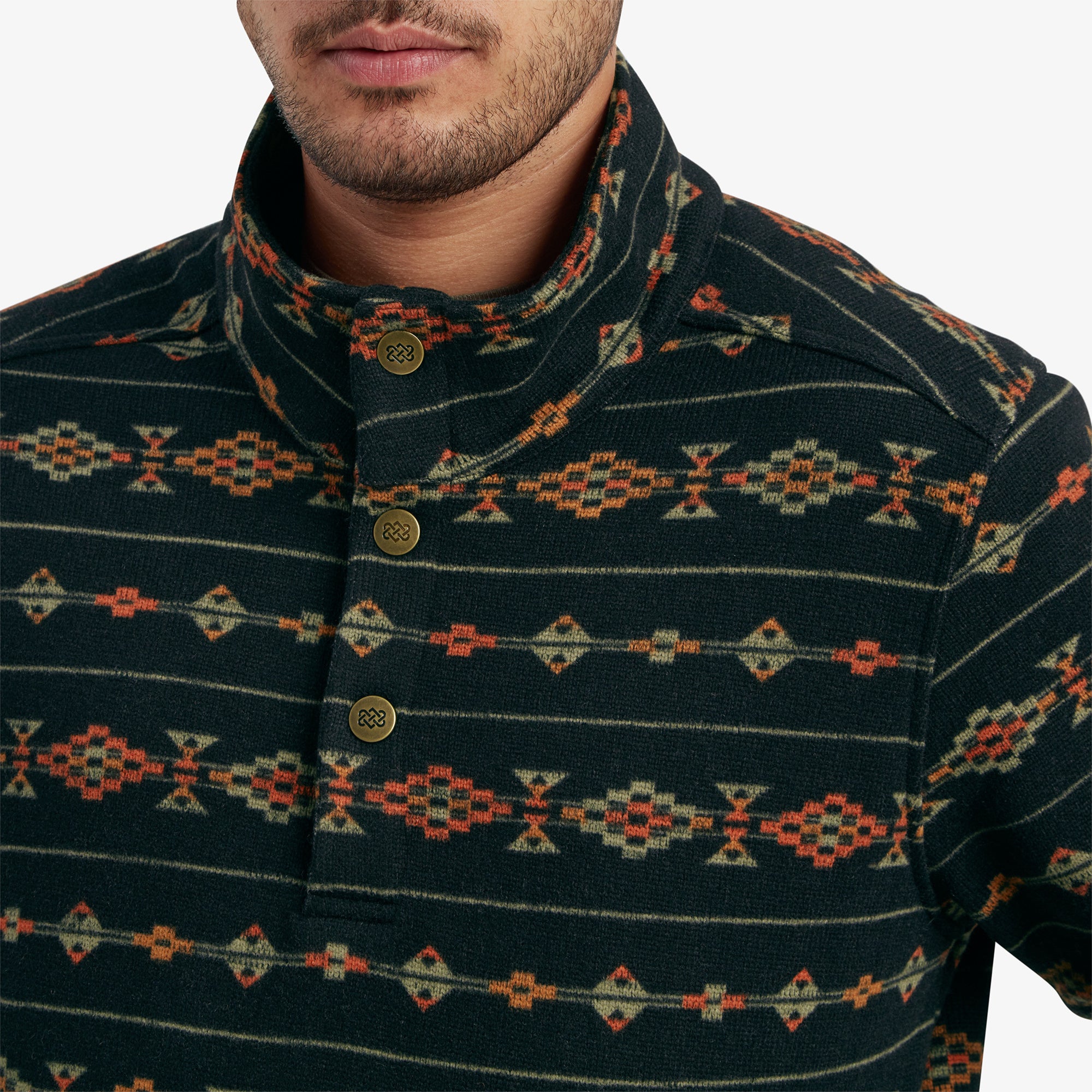 A close-up of the high collar of the Sherpa Adventure Gear Bhutan Pullover in Black, highlighting the three metallic buttons engraved with a minimalist design and the colorful geometric pattern on the fabric.