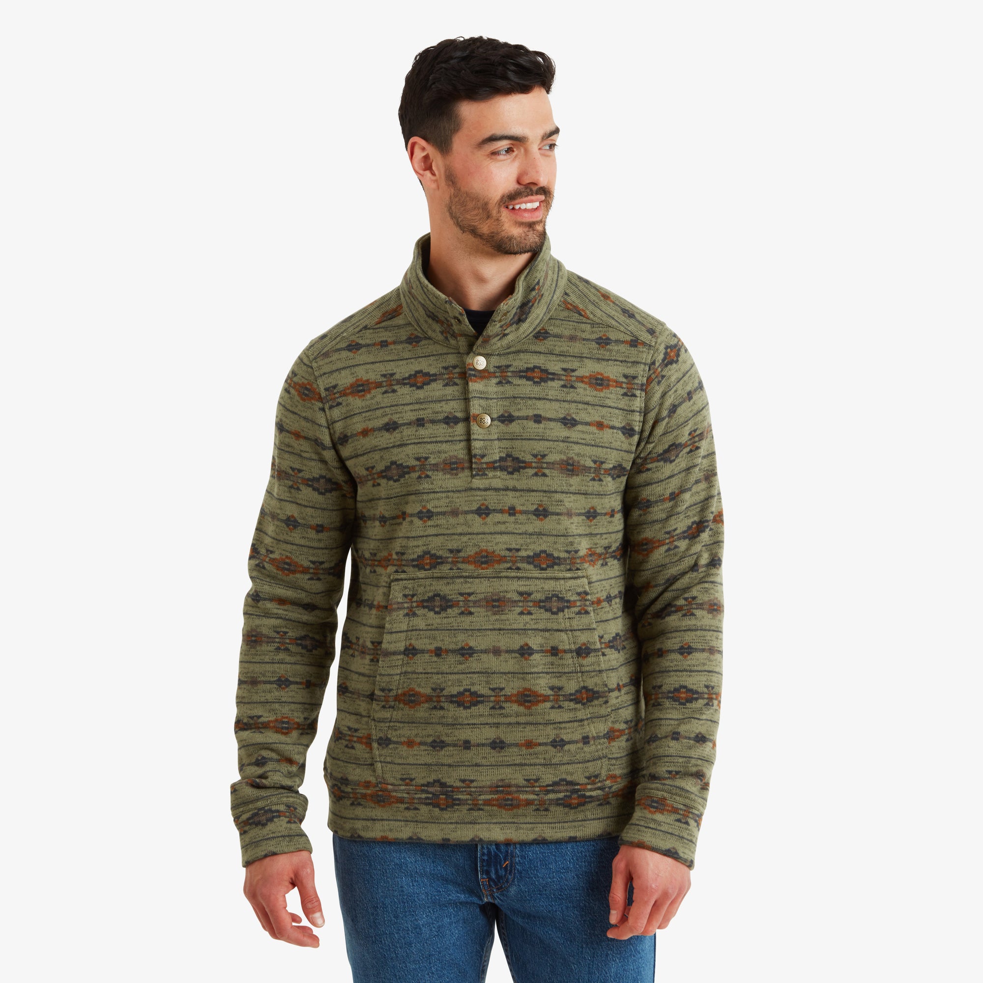 A man wears a Sherpa Adventure Gear Bhutan Pullover in Green with intricate multicolor patterns, including orange and navy details. The pullover has a high-buttoned neckline with three visible buttons, giving it a classic yet stylish look. The man smiles slightly and has one hand relaxed by his side. The background is plain white, making the pullover's detailed design stand out.