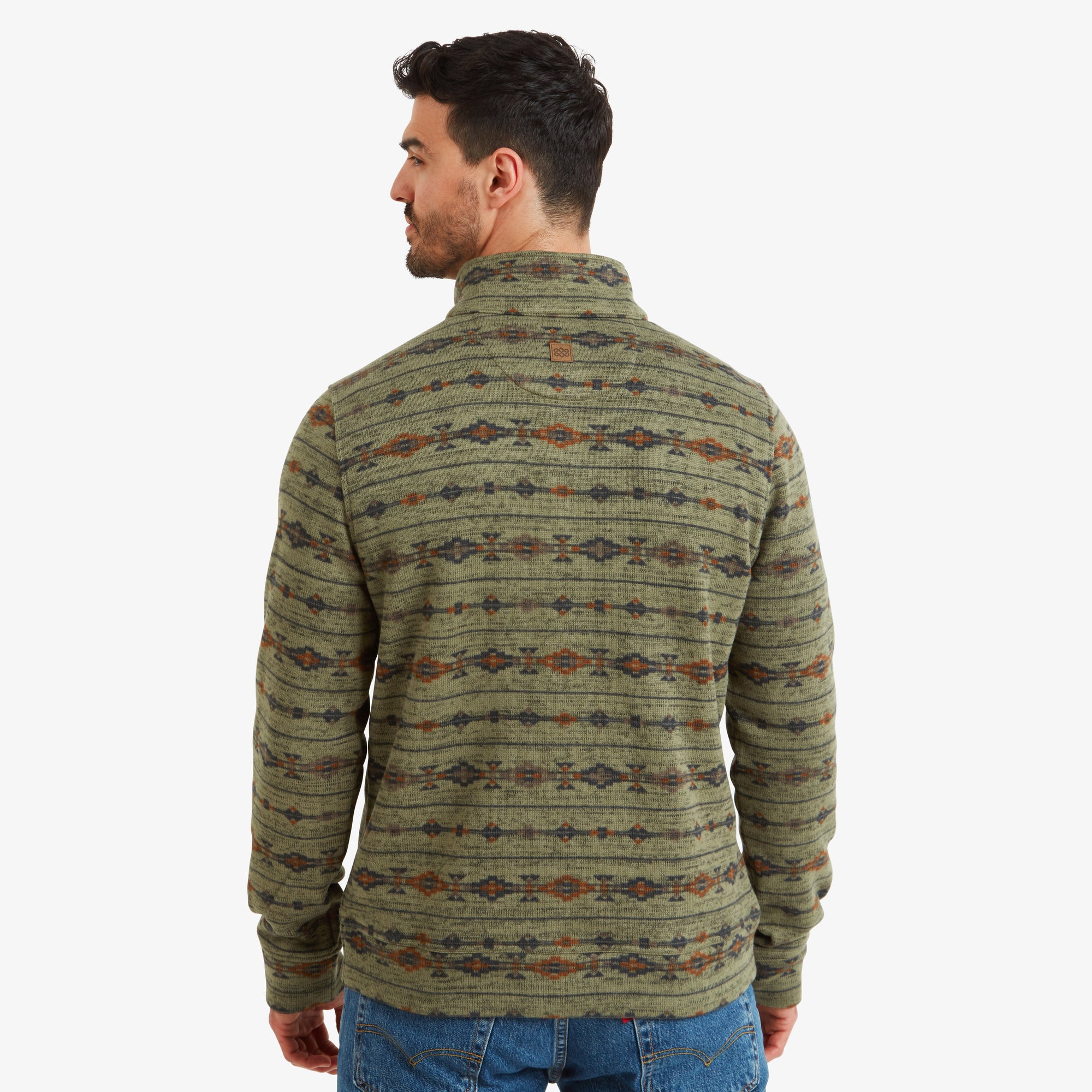 A back view of the Sherpa Adventure Gear Bhutan Pullover in Green displays the continuous design across the shoulders and back. The high neckline is clearly visible, along with a small stitched logo near the center of the upper back. The man’s relaxed pose shows the garment’s comfort and casual fit.