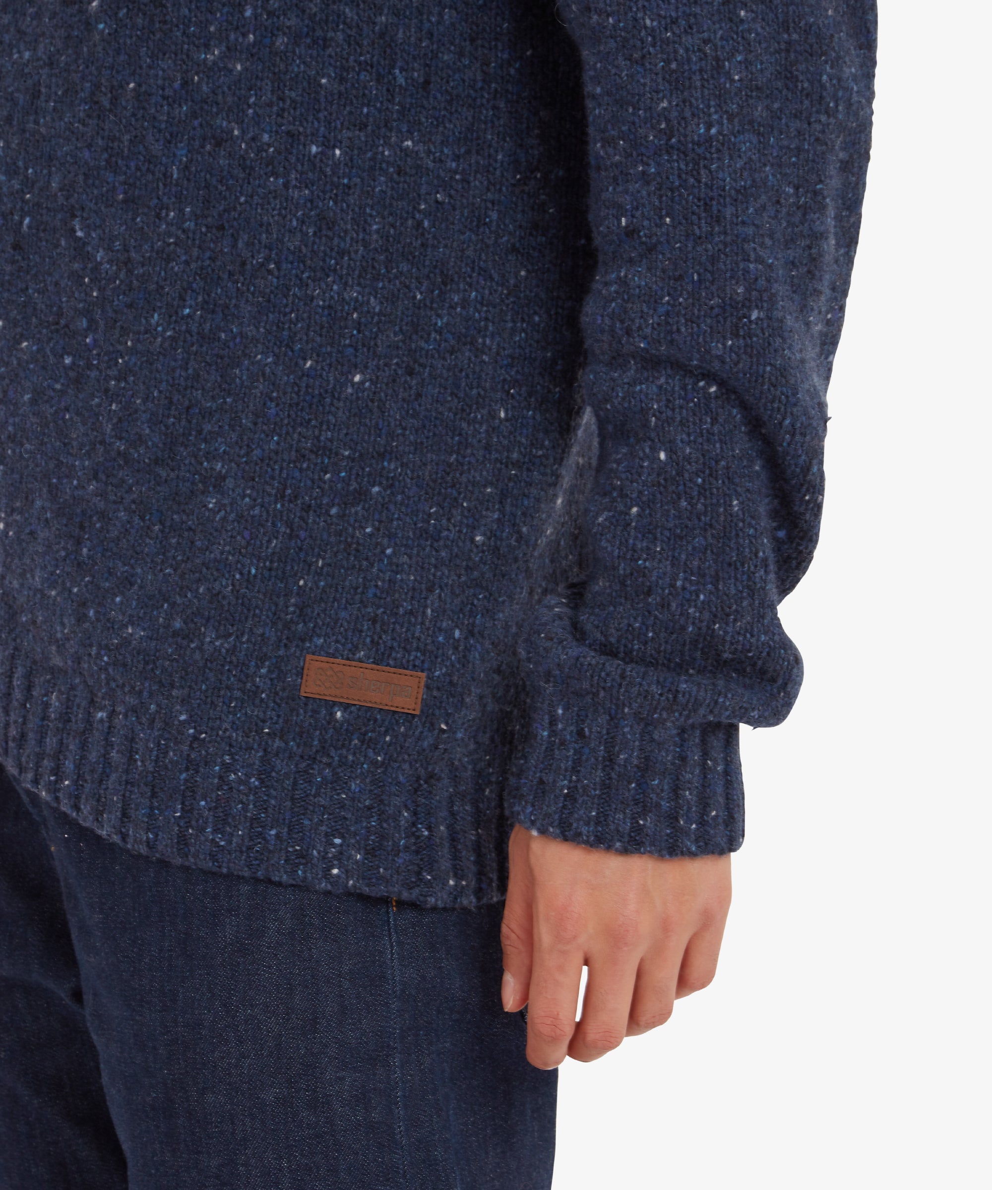 A close-up shot of the Sherpa Adventure Gear Dumji Full Zip in Blue's sleeve hem, showing the speckled knit fabric texture. A small leather Sherpa logo patch is visible near the hem, highlighting the branding.