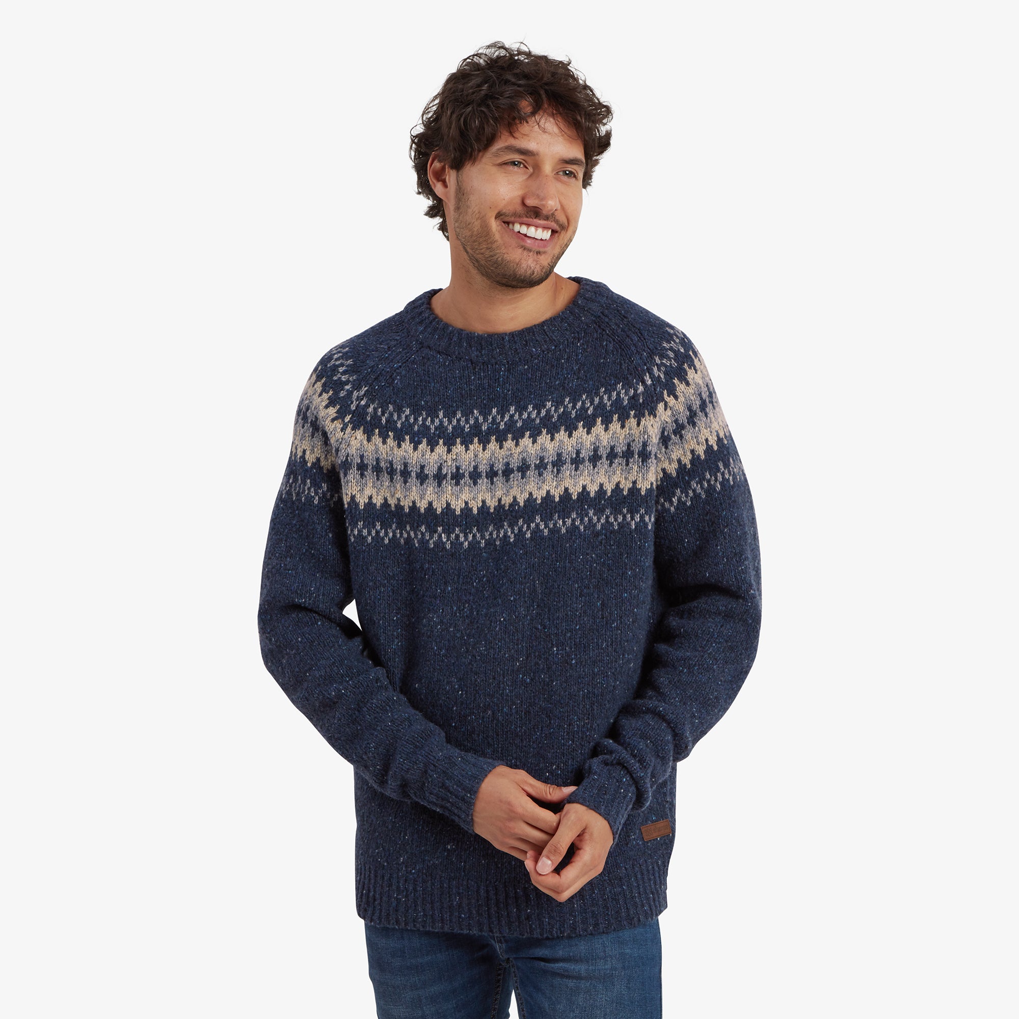 A man is wearing a Sherpa Adventure Gear Dumji Sweater in Blue featuring a traditional geometric pattern across the chest and upper arms in shades of cream and gray. The sweater has a classic crew neck and a slightly textured knit. The man smiles warmly with hands relaxed, showcasing the casual yet cozy fit.