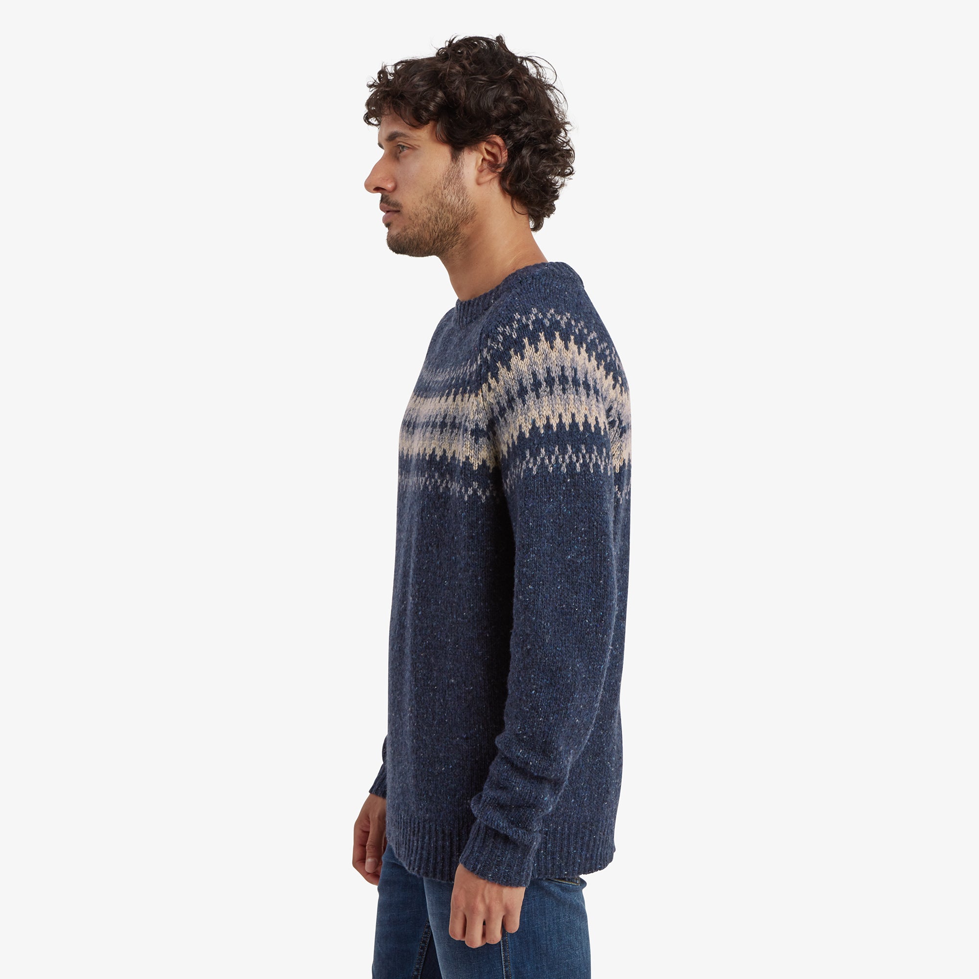 A side view of the man highlights the Sherpa Adventure Gear Dumji Sweater in Blue’s straight fit and pattern continuity along the sleeves and body. The textured knit and rounded neckline are visible, emphasising the garment's relaxed yet tailored look.