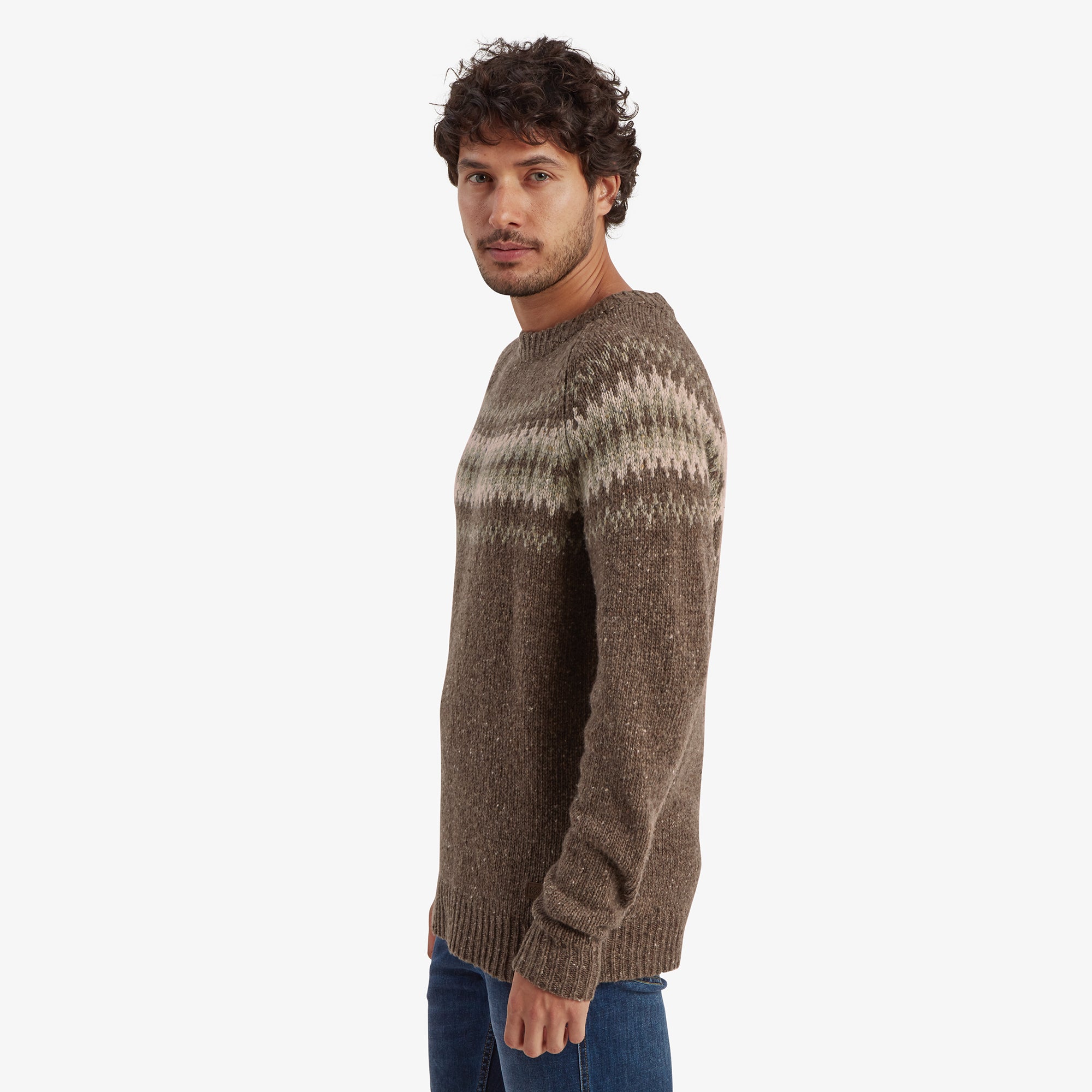 A side-profile view of the model wearing the Sherpa Adventure Gear Dumji Sweater in Brown, showcasing the fit and thickness of the fabric. The Fair Isle pattern extends across the chest and upper arms, while the rest of the sweater is a speckled brown knit. He has a neutral facial expression as he gazes toward the camera.