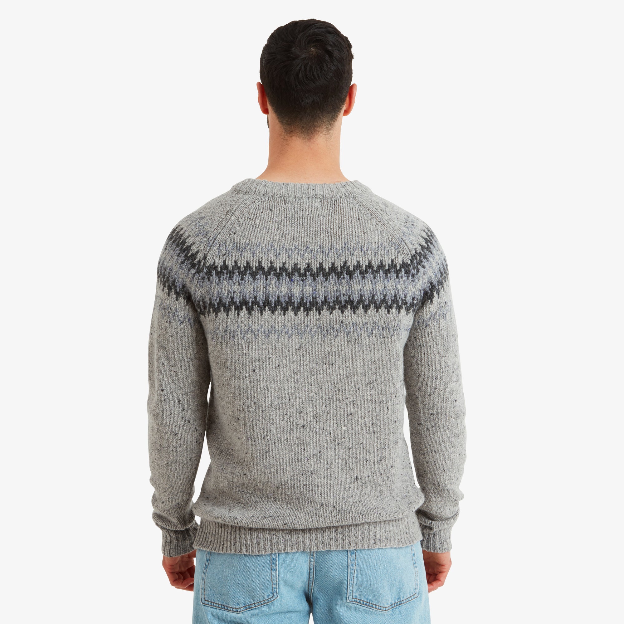 The model turned to display the back of the Sherpa Adventure Gear Dumji Sweater in Brown. The same geometric pattern continues across the upper back, with a clean, minimal design on the rest of the knit. The natural texture and fine detailing of the material are evident in this angle.