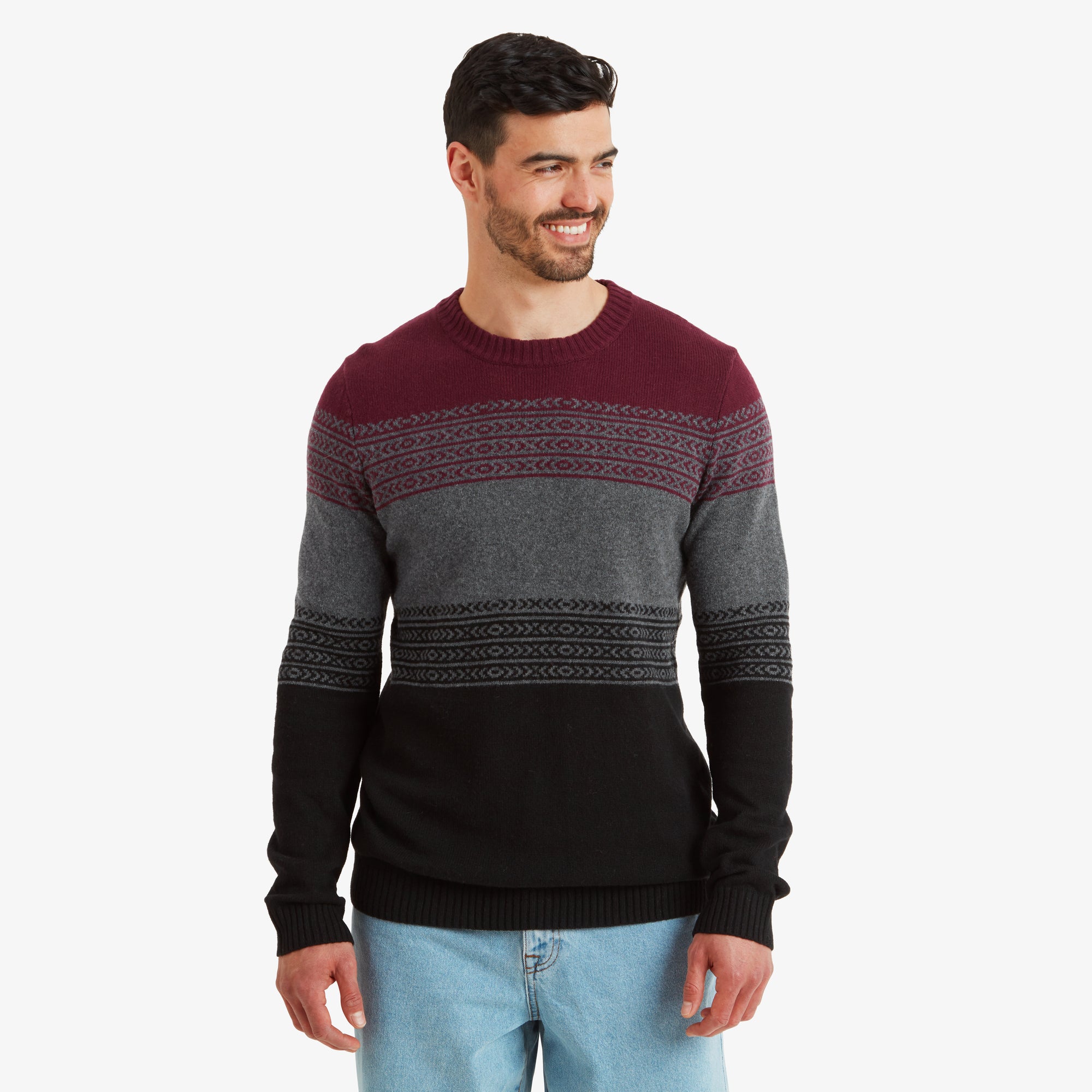 A man wearing a Sherpa Adventure Gear Hatauda Crew in Grey in a striped design with maroon, gray, and black horizontal bands. He is smiling and standing casually, showcasing the front of the sweater.