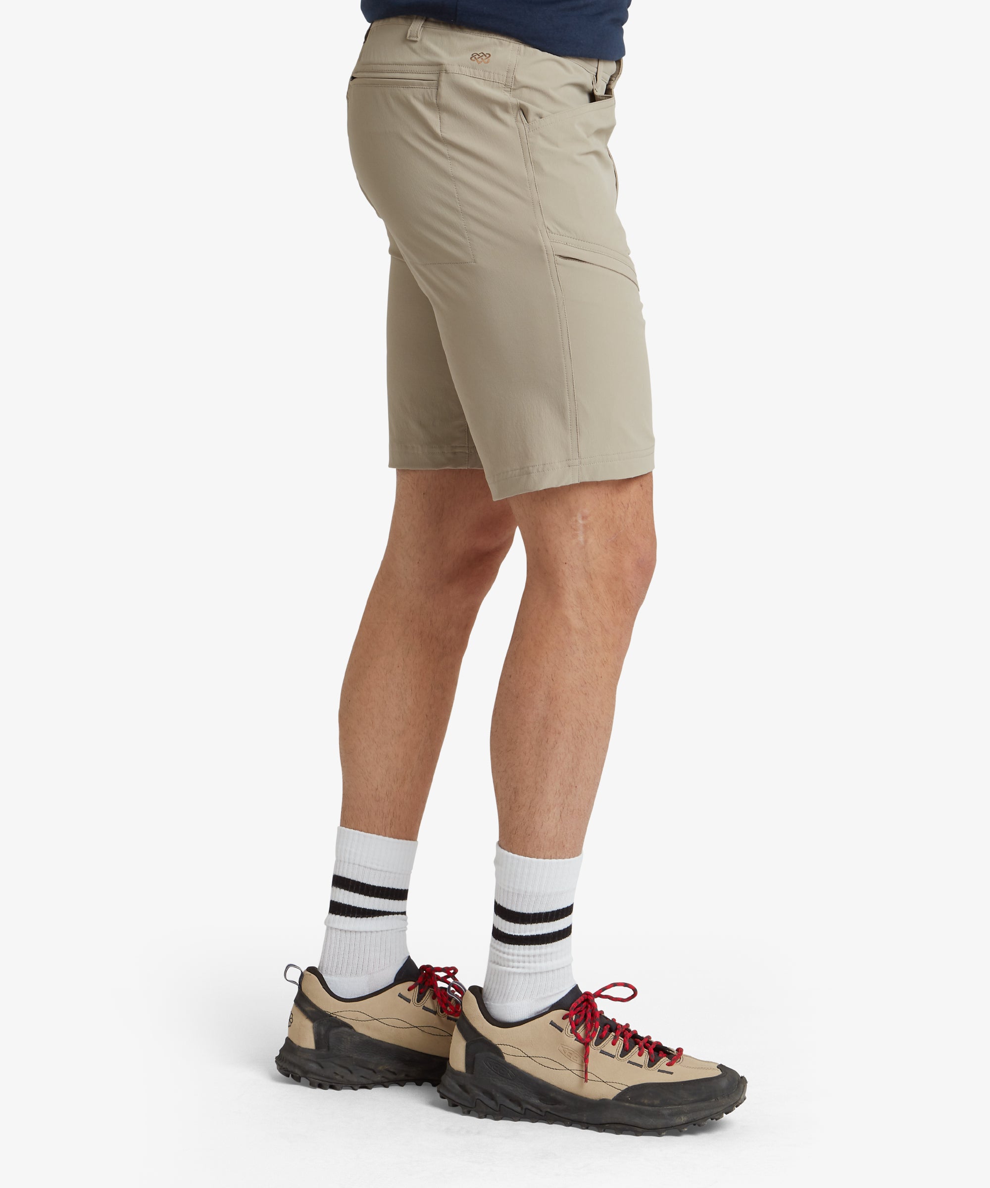 The rear view of the Sherpa Adventure Gear Jamyang Shorts in Beige reveals back pocket detailing and the smooth fit around the waist and hips. The model's posture accentuates the tailored design of the shorts, providing a full perspective of their structure.