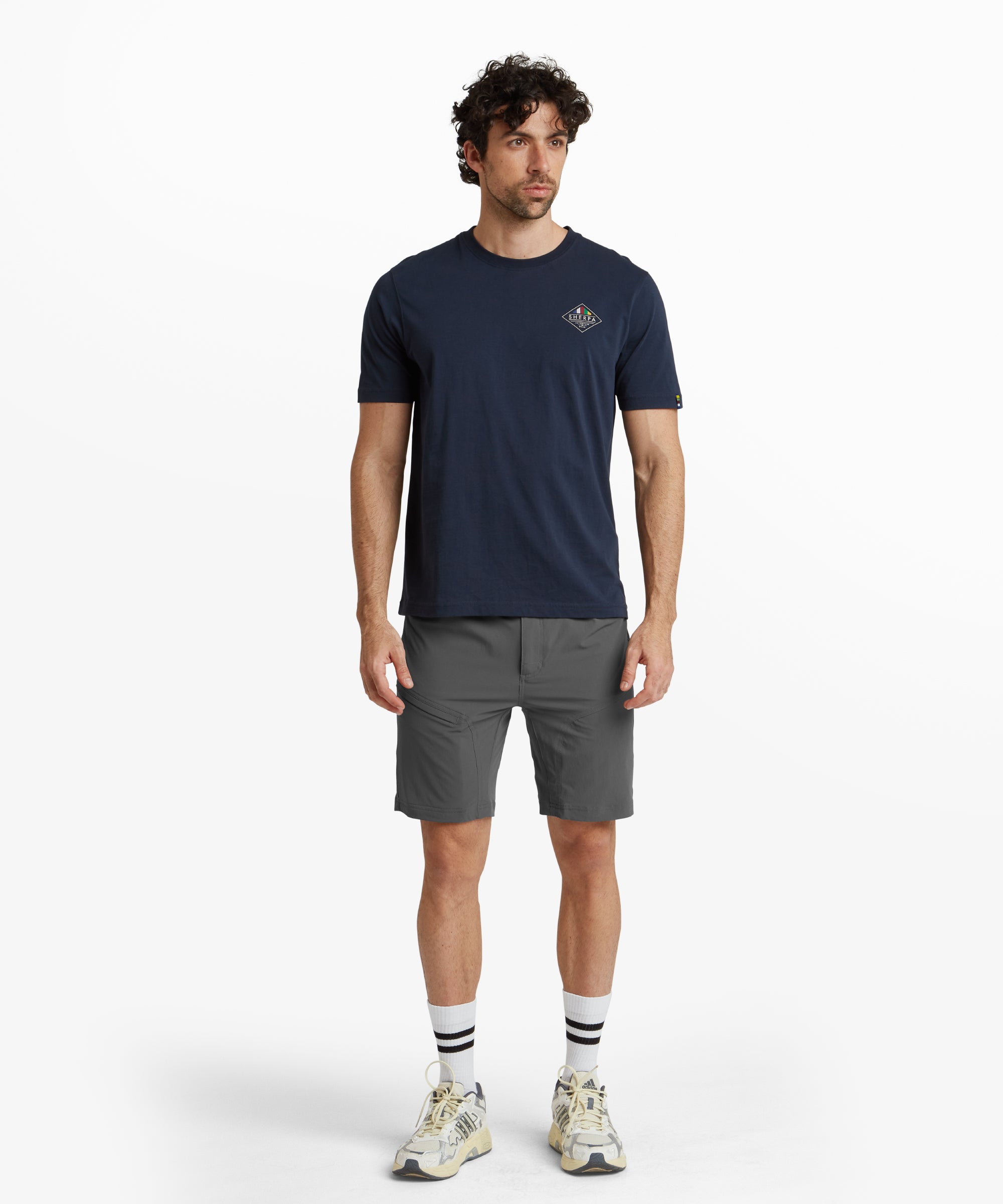 A slightly angled side view of the Sherpa Adventure Gear Jamyang Shorts in Grey, demonstrating the modern fit and functional pockets on each side. The stitching details emphasise the durable construction. The outfit is complemented by white trainers, reflecting a casual and sporty look.