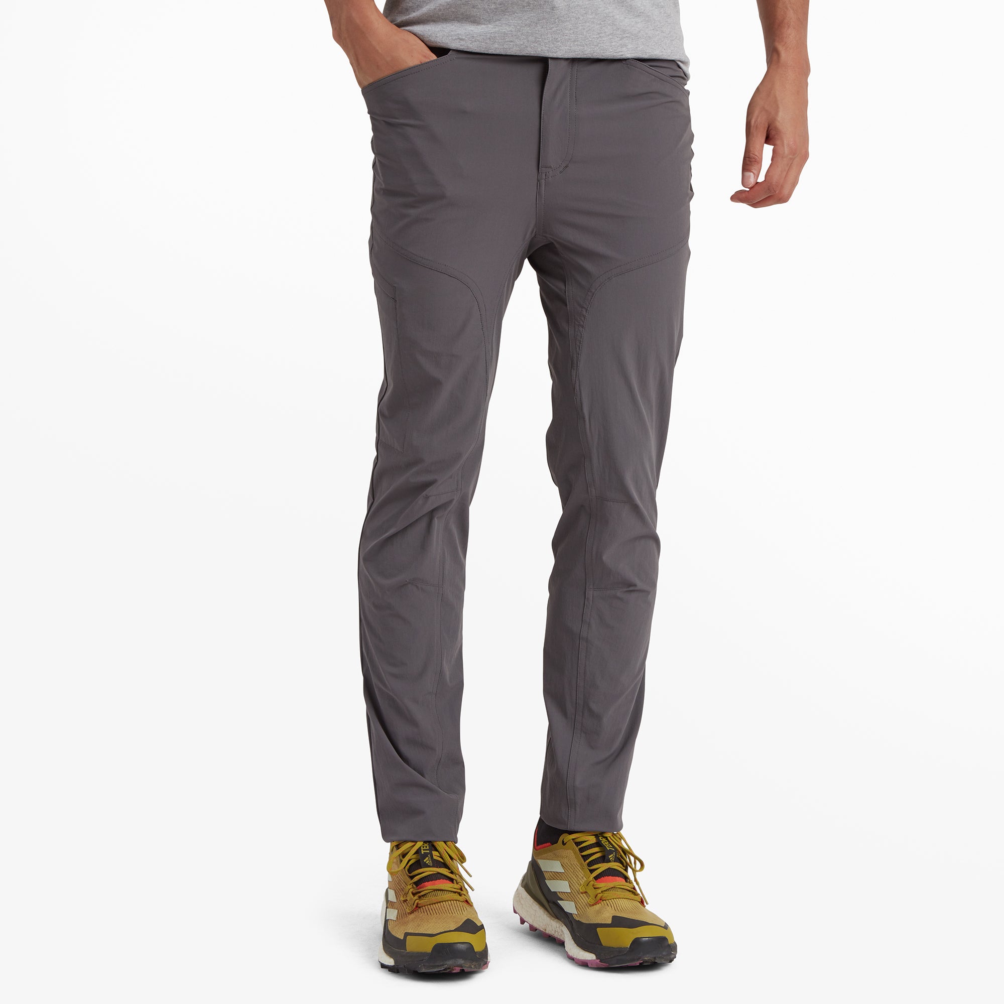 A close-up view of a pair of Sherpa Adventure Gear Jamyang trousers in Grey showcasing the front pockets and fine stitching details. The model is wearing the trousers with mustard-colored hiking shoes, emphasising a rugged and casual look. The lightweight, flexible material is evident in the fit and texture.