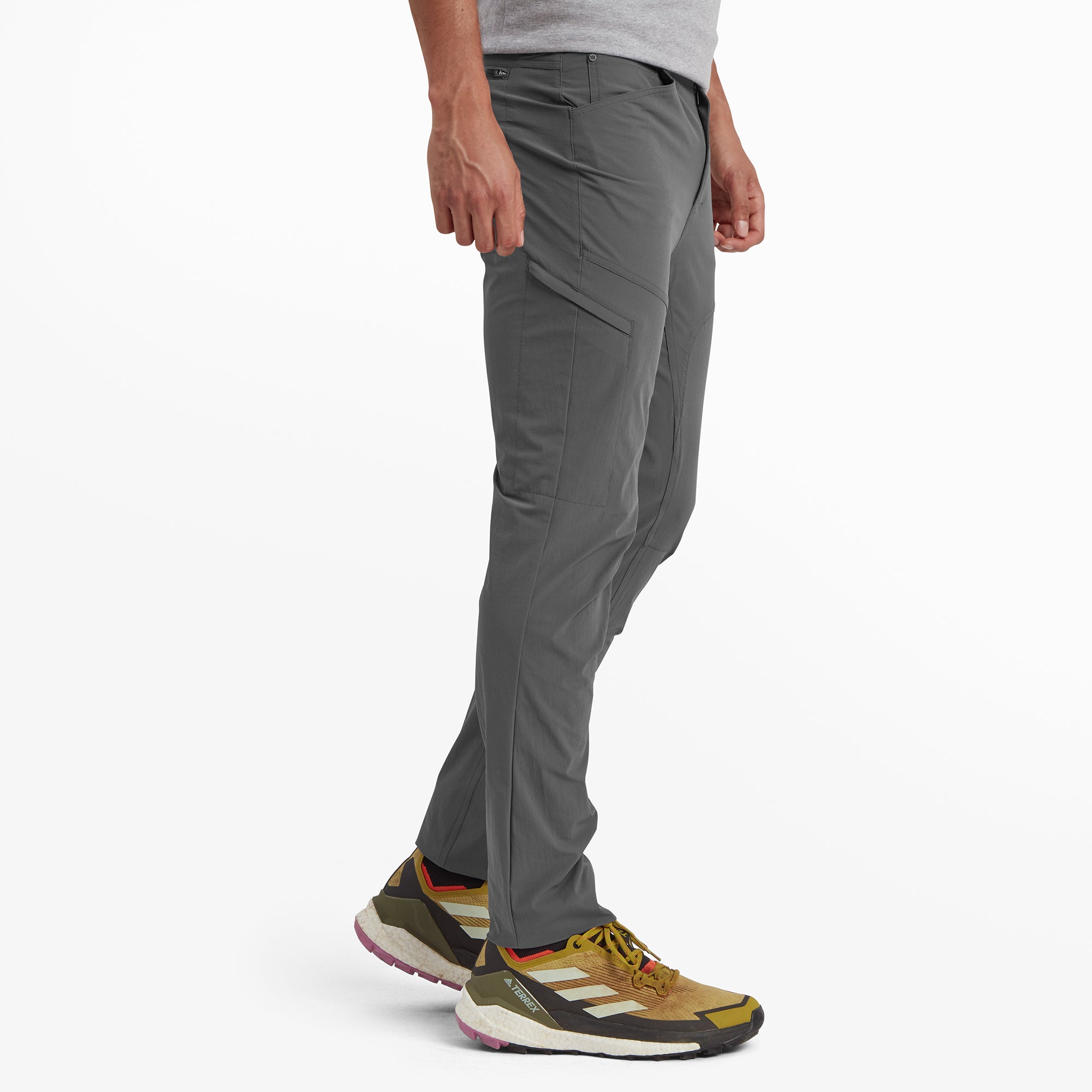 A side profile of the Sherpa Adventure Gear Jamyang trousers in Grey showing the tailored cut and functional design, including a zippered side pocket. The model is mid-step, giving a dynamic view of the trousers' mobility and comfort.