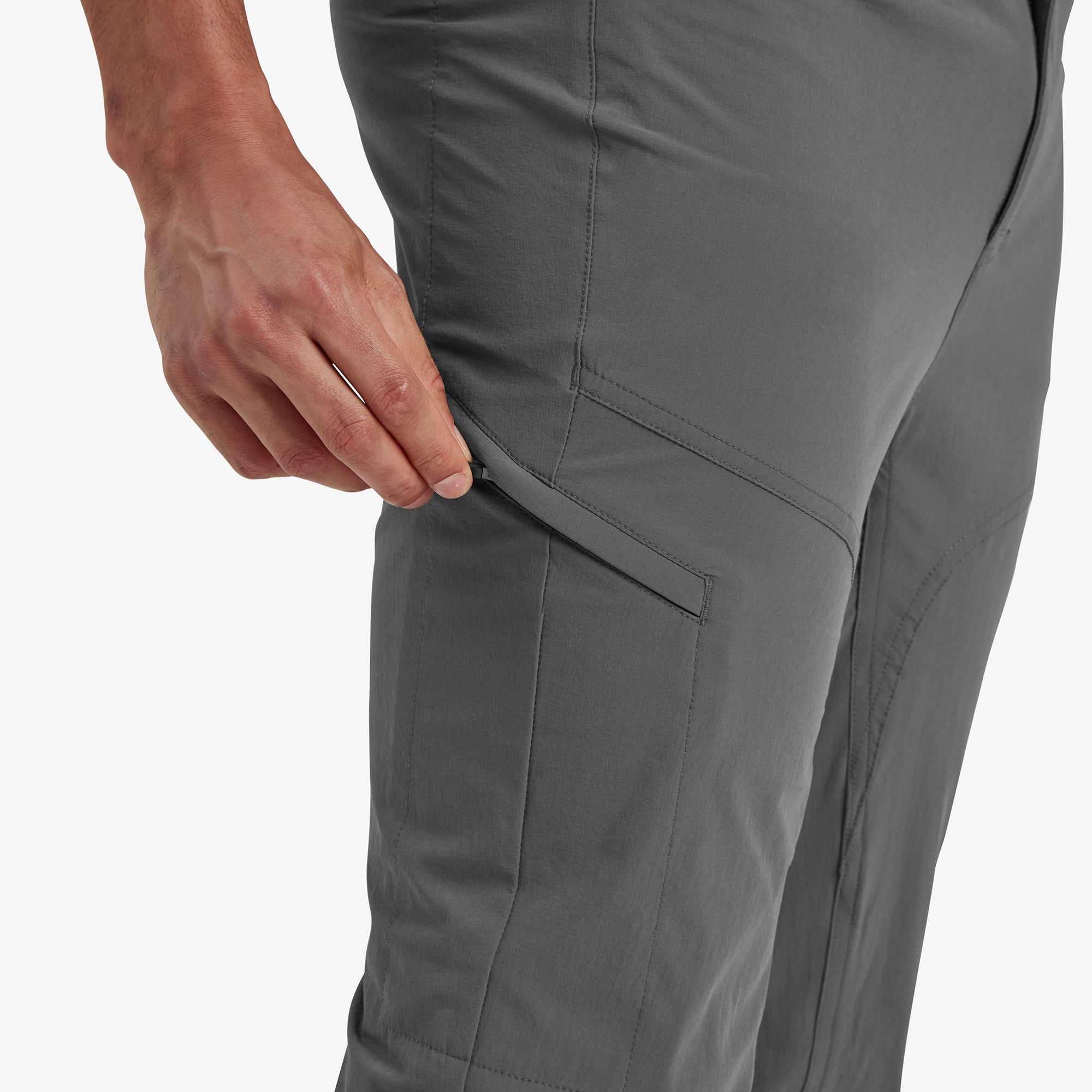 A detailed close-up of the side pocket of the Sherpa Adventure Gear Jamyang trousers in Grey, with the model's hand demonstrating the zipper functionality. The image highlights the practicality of the design for storing small essentials during outdoor activities.