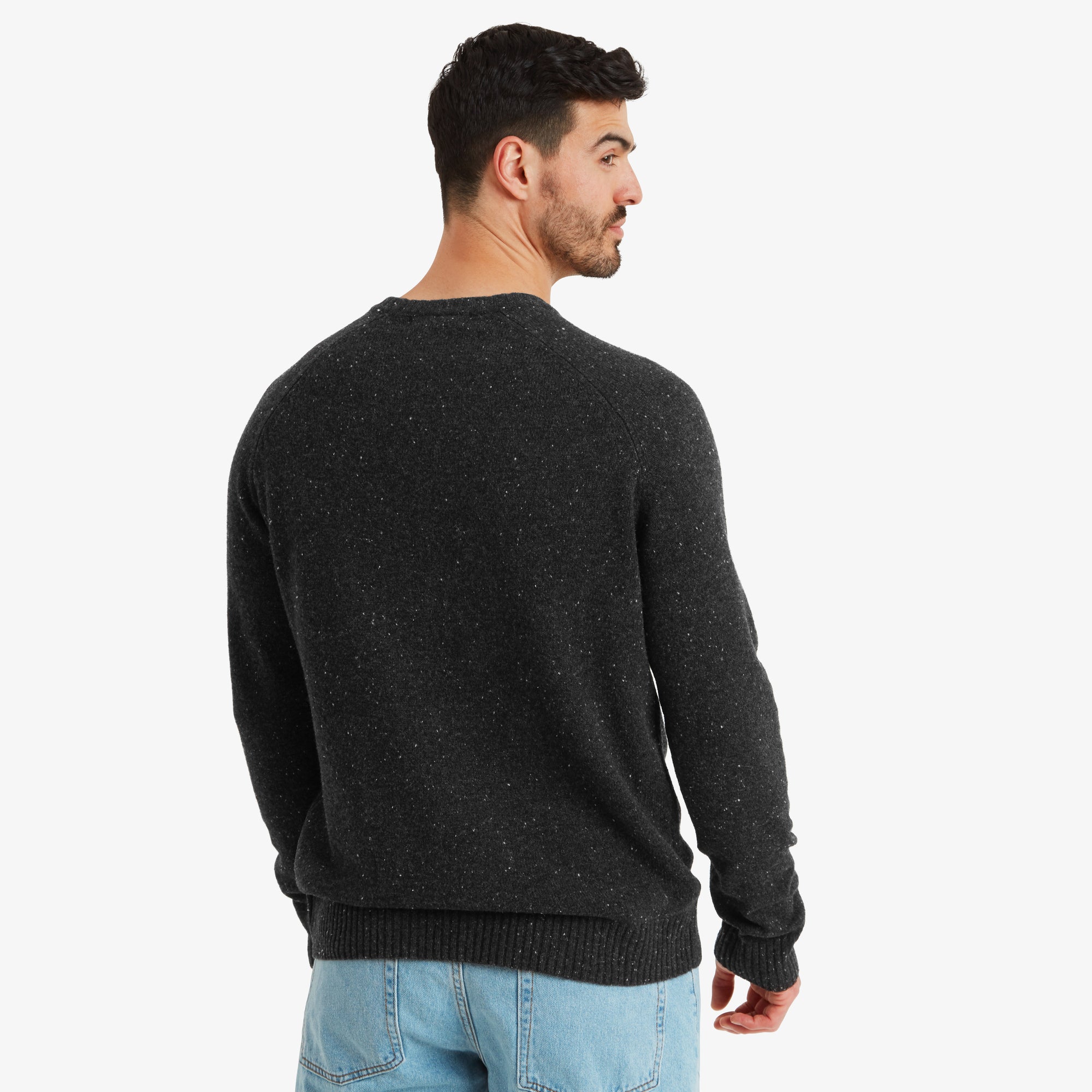 A rear perspective of the Sherpa Adventure Gear Kangtega Crew Sweater in Black, showing its seamless design with no additional details, creating a clean and simple aesthetic. The back hemline rests naturally against the model's light-wash jeans.