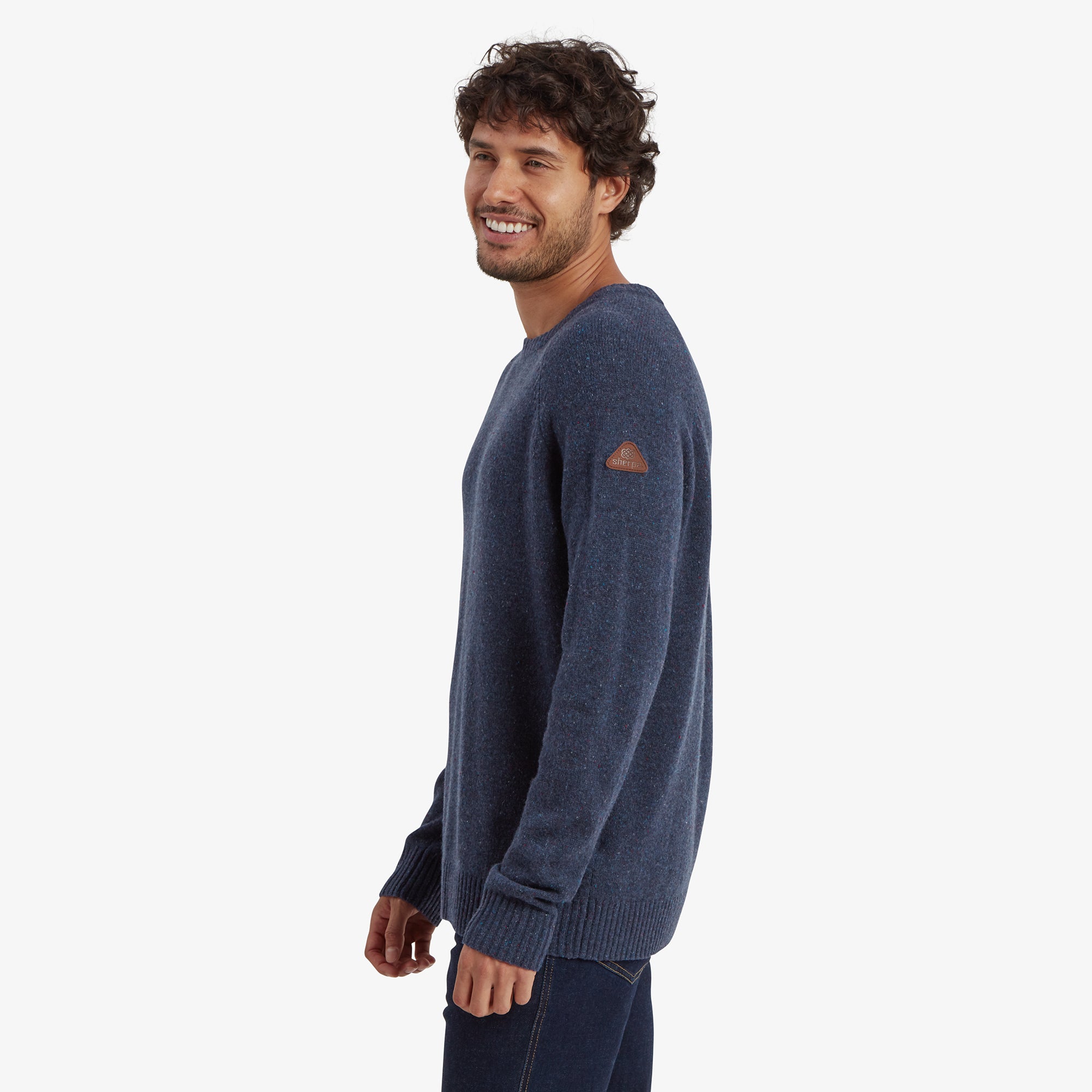 Side profile of the model showcasing the Sherpa Adventure Gear Kangtega Crew Sweater in Blue's comfortable fit and seamless design. The left sleeve features a small leather patch with branding, adding a subtle design detail.