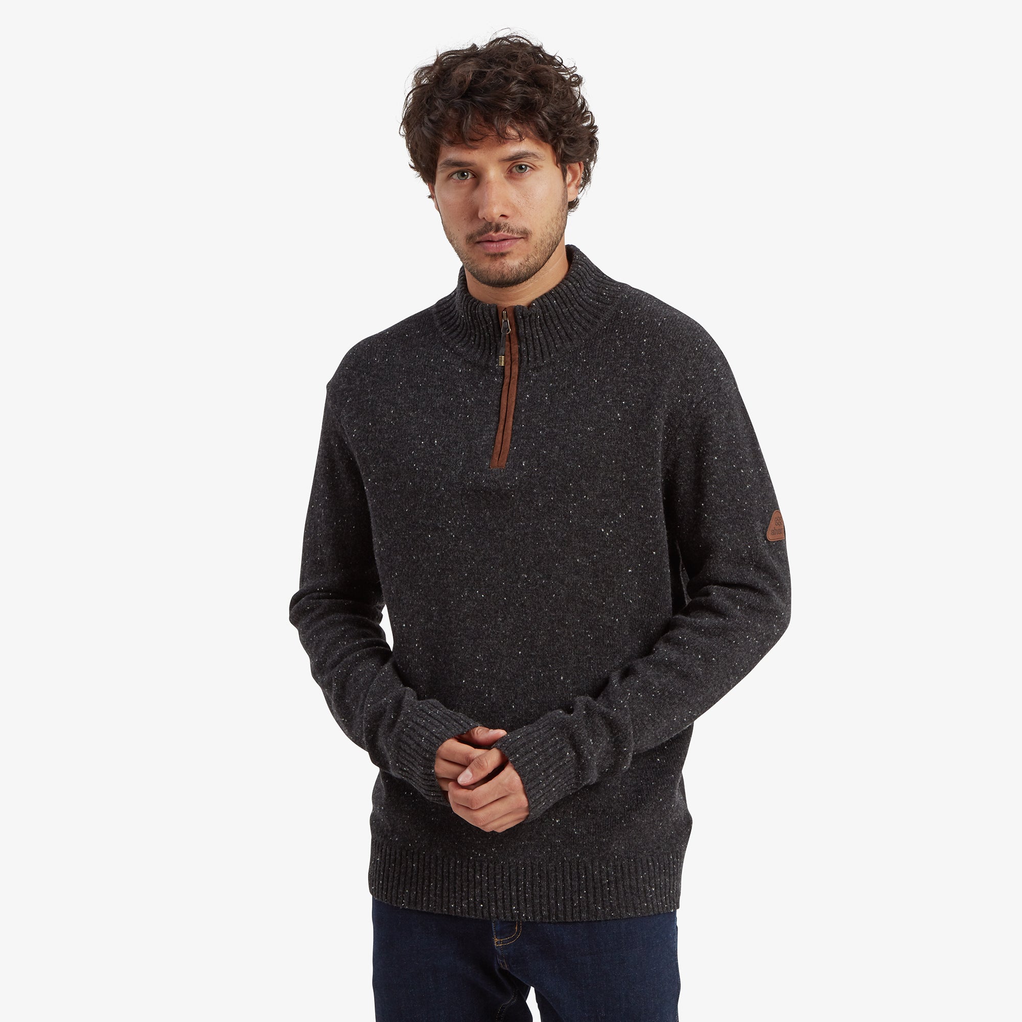 A man wearing a Sherpa Adventure Gear Kangtega Quarter Zip Sweater in Black, standing with a neutral expression. The sweater features a speckled knit design, a ribbed collar, cuffs, and hem, and a suede-like zipper pull. He pairs it with dark denim jeans for a casual look.