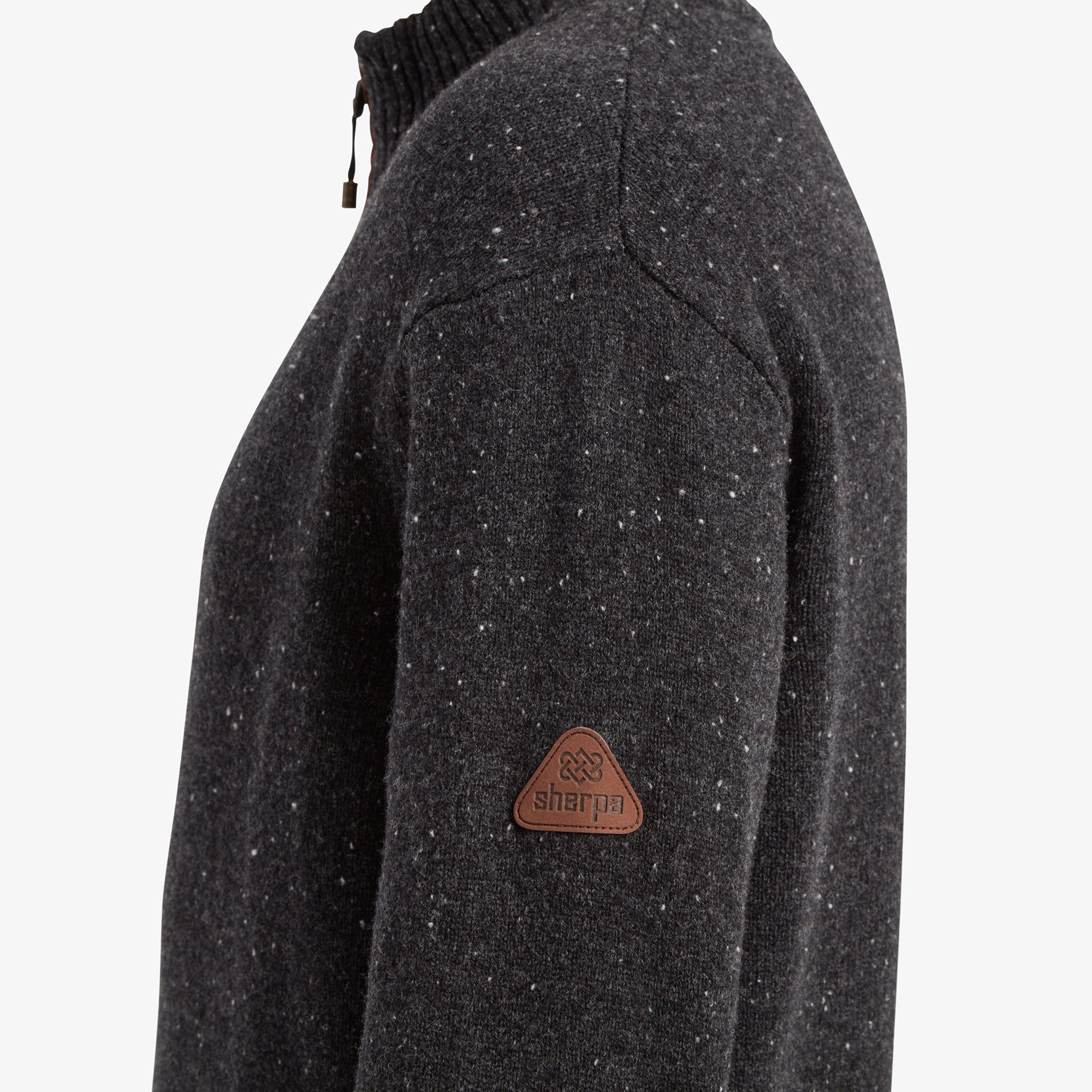 A close-up of the Sherpa logo patch on the Sherpa Adventure Gear Kangtega Quarter Zip Sweater in Black's sleeve. The logo is a small triangular leather patch embossed with the Sherpa branding, sewn neatly onto the speckled knit fabric.